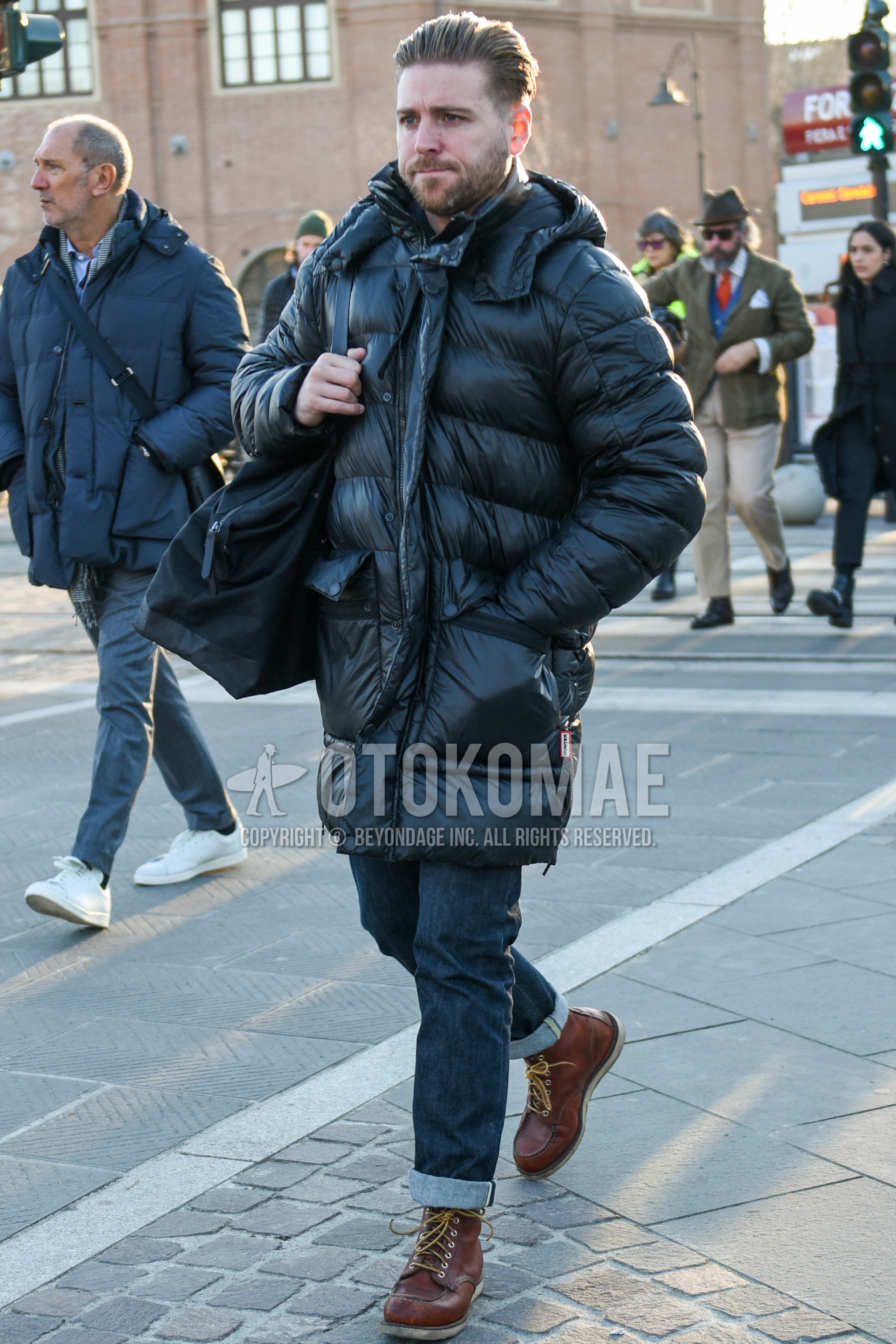 Men's winter outfit with black plain down jacket, black plain hooded coat, navy plain denim/jeans, brown work boots, black plain briefcase/handbag.
