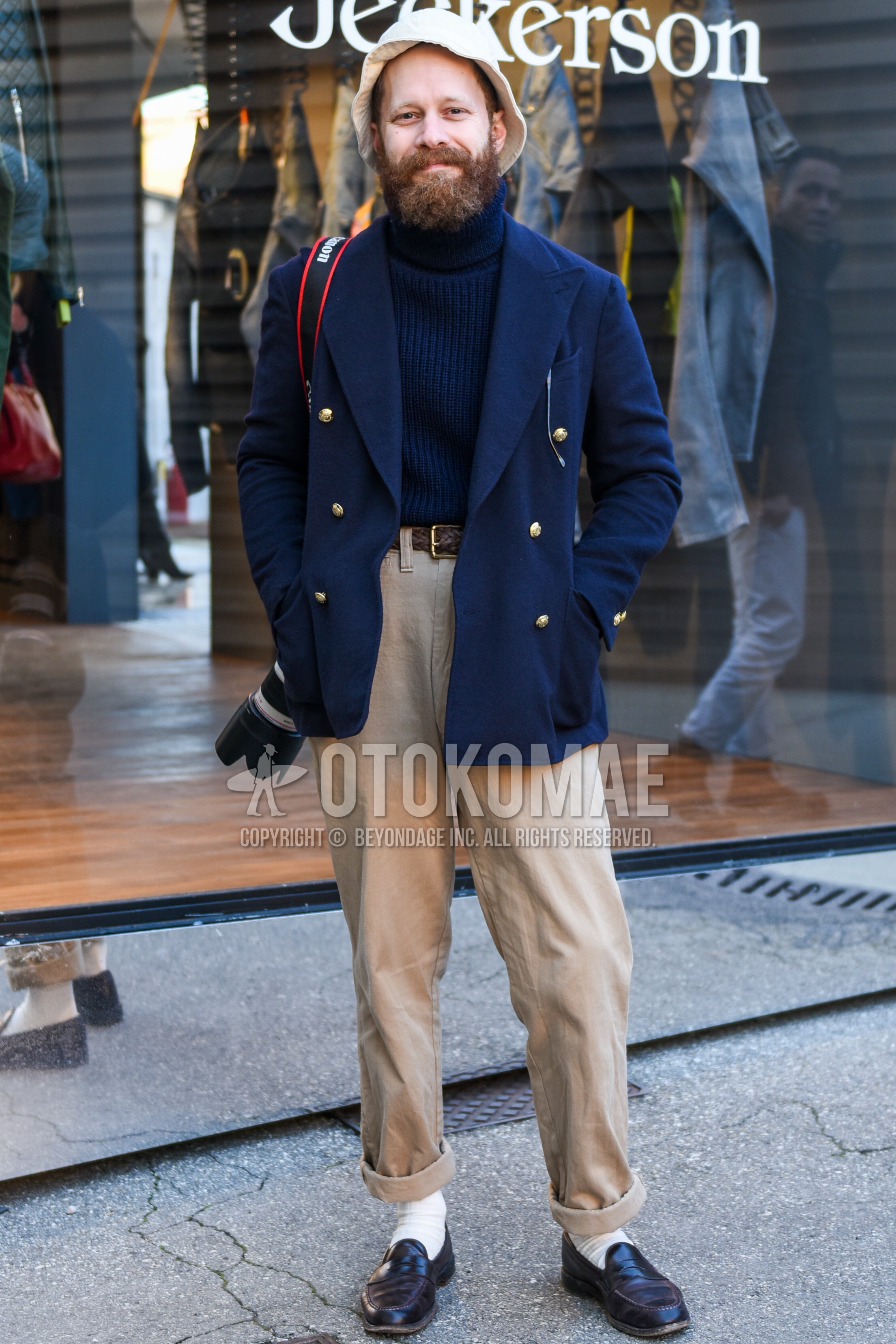 Men's autumn winter outfit with navy plain tailored jacket, navy plain turtleneck knit, brown plain braided belt, brown plain leather belt, beige plain chinos, white plain socks, black coin loafers leather shoes.