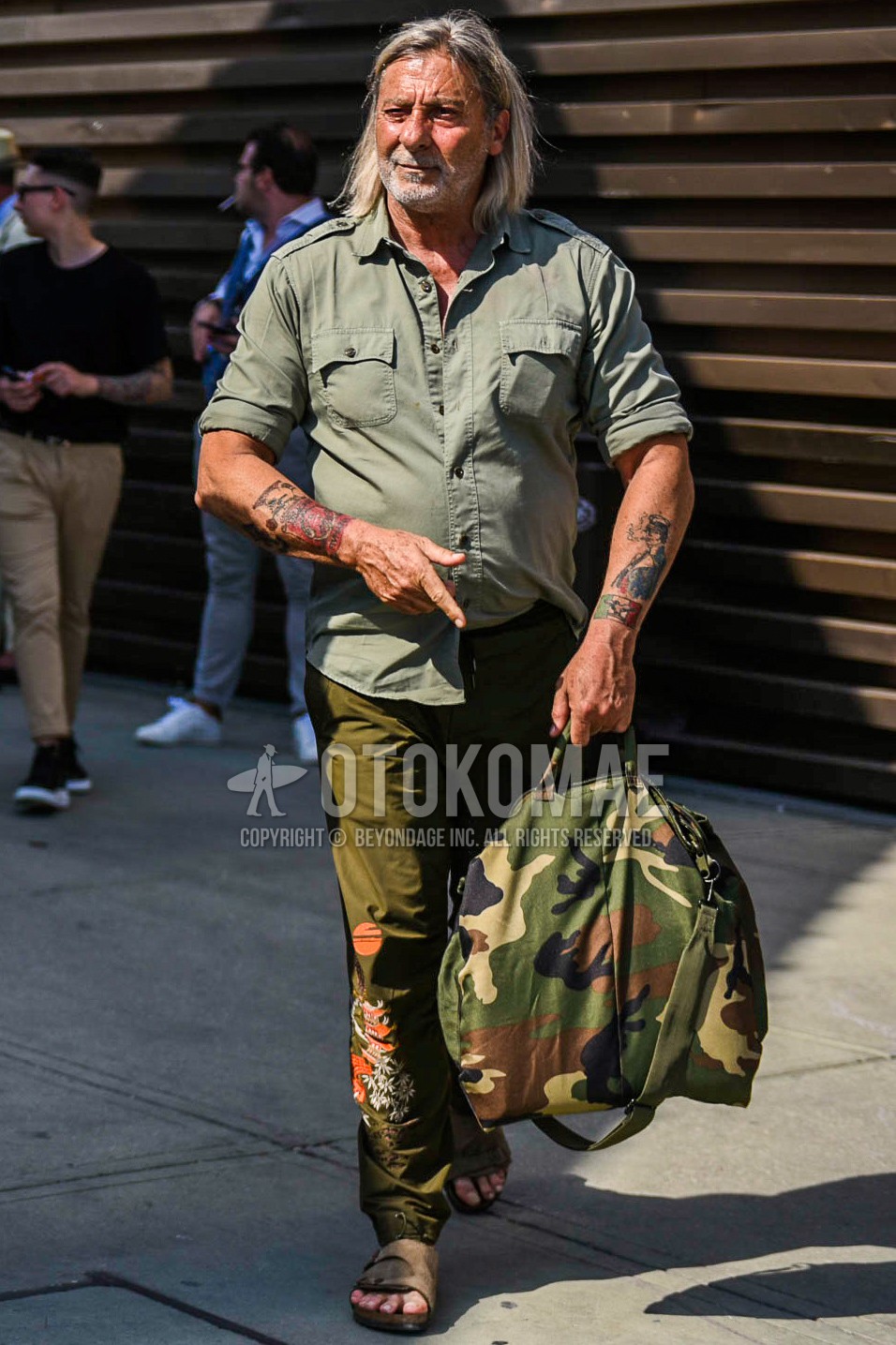 Men's spring summer autumn outfit with olive green plain shirt, olive green bottoms jogger pants/ribbed pants, brown leather sandals, green camouflage boston bag.