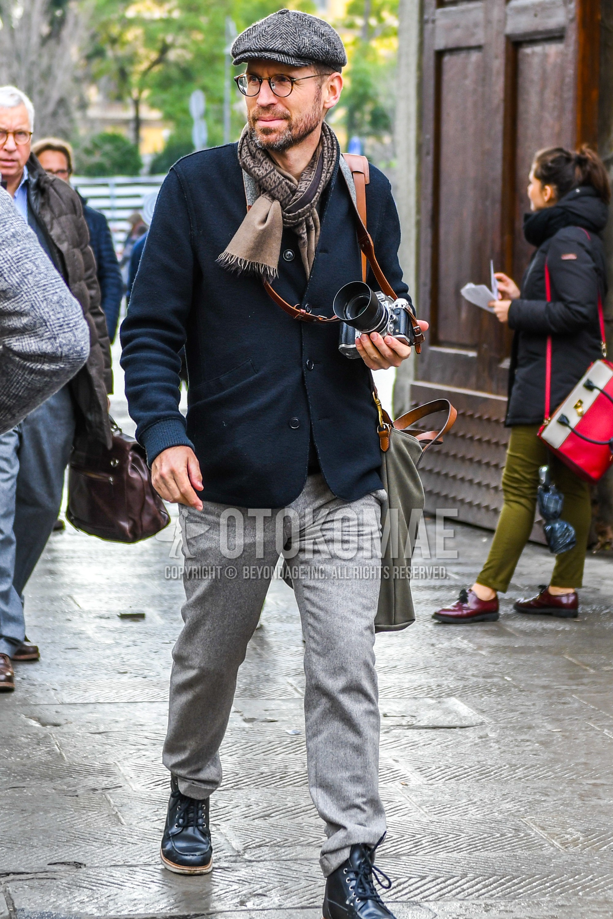 Men's autumn outfit with gray plain cap, plain glasses, brown scarf scarf, black plain cardigan, gray plain slacks, black  boots, gray plain shoulder bag.