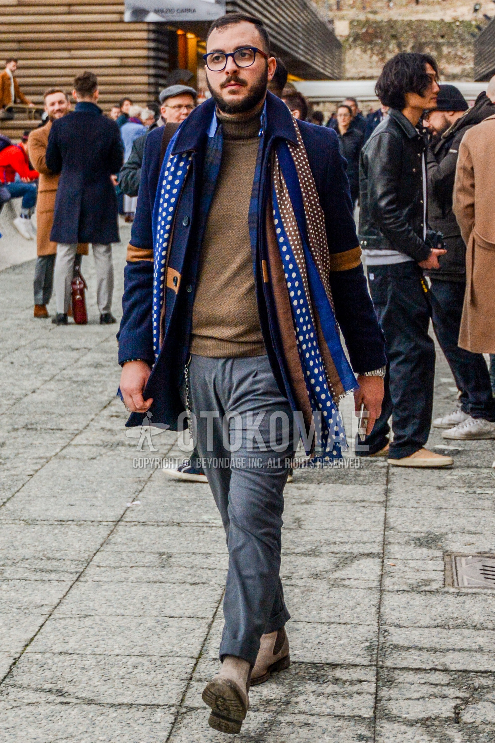Men's winter outfit with blue plain glasses, blue brown dots scarf, navy plain stenkarrer coat, beige plain turtleneck knit, gray plain slacks, beige side-gore boots.