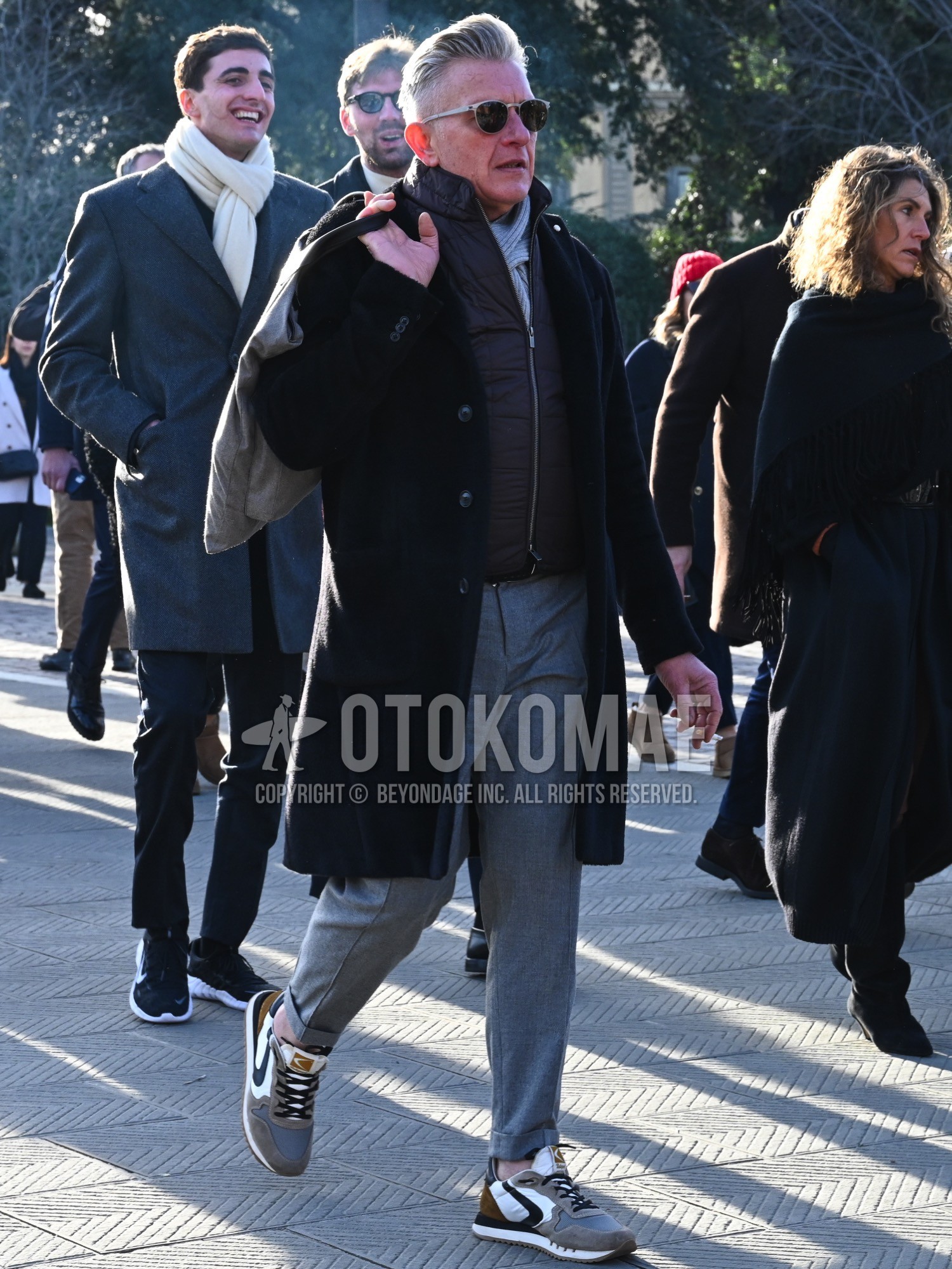 Men's autumn winter outfit with gray plain sunglasses, gray plain scarf, black plain chester coat, dark gray plain casual vest, gray plain slacks, gray low-cut sneakers.