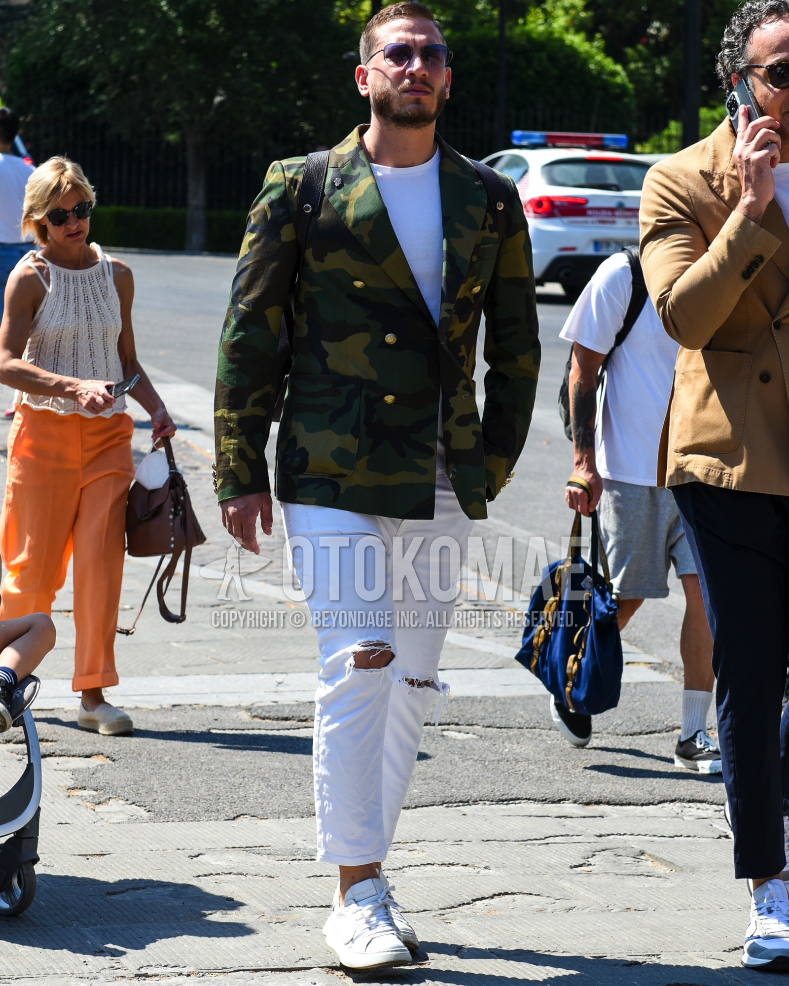 Men's spring summer outfit with black plain sunglasses, olive green camouflage tailored jacket, white plain t-shirt, white plain damaged jeans, white plain cropped pants, white low-cut sneakers, black plain backpack.
