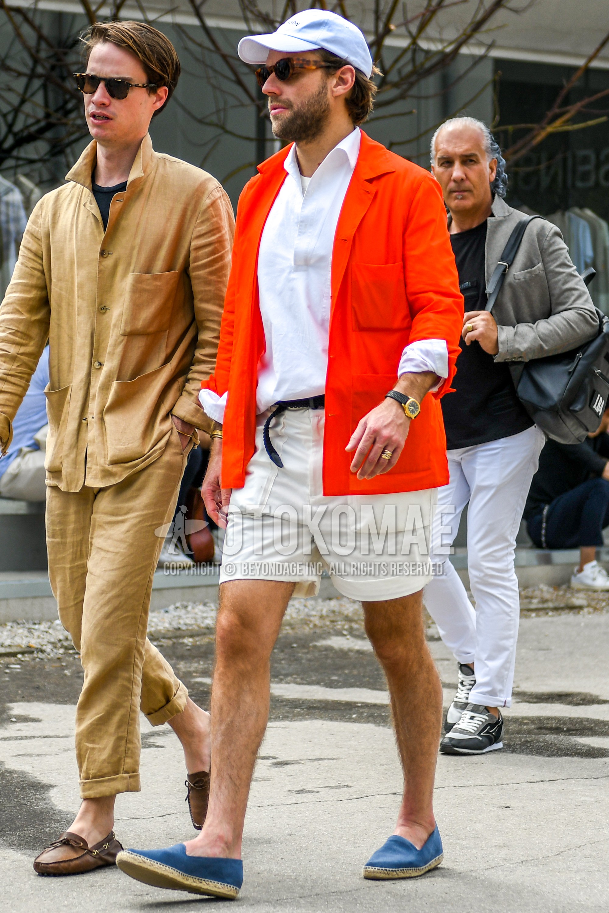 Men's spring summer autumn outfit with white plain baseball cap, orange plain shirt jacket, white plain shirt, black plain leather belt, beige plain short pants, blue espadrille.