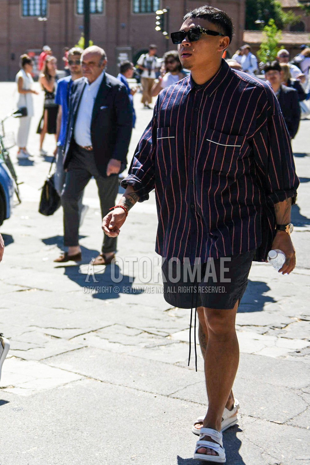 Men's spring summer outfit with black plain sunglasses, navy stripes shirt, black plain short pants, white sport sandals.