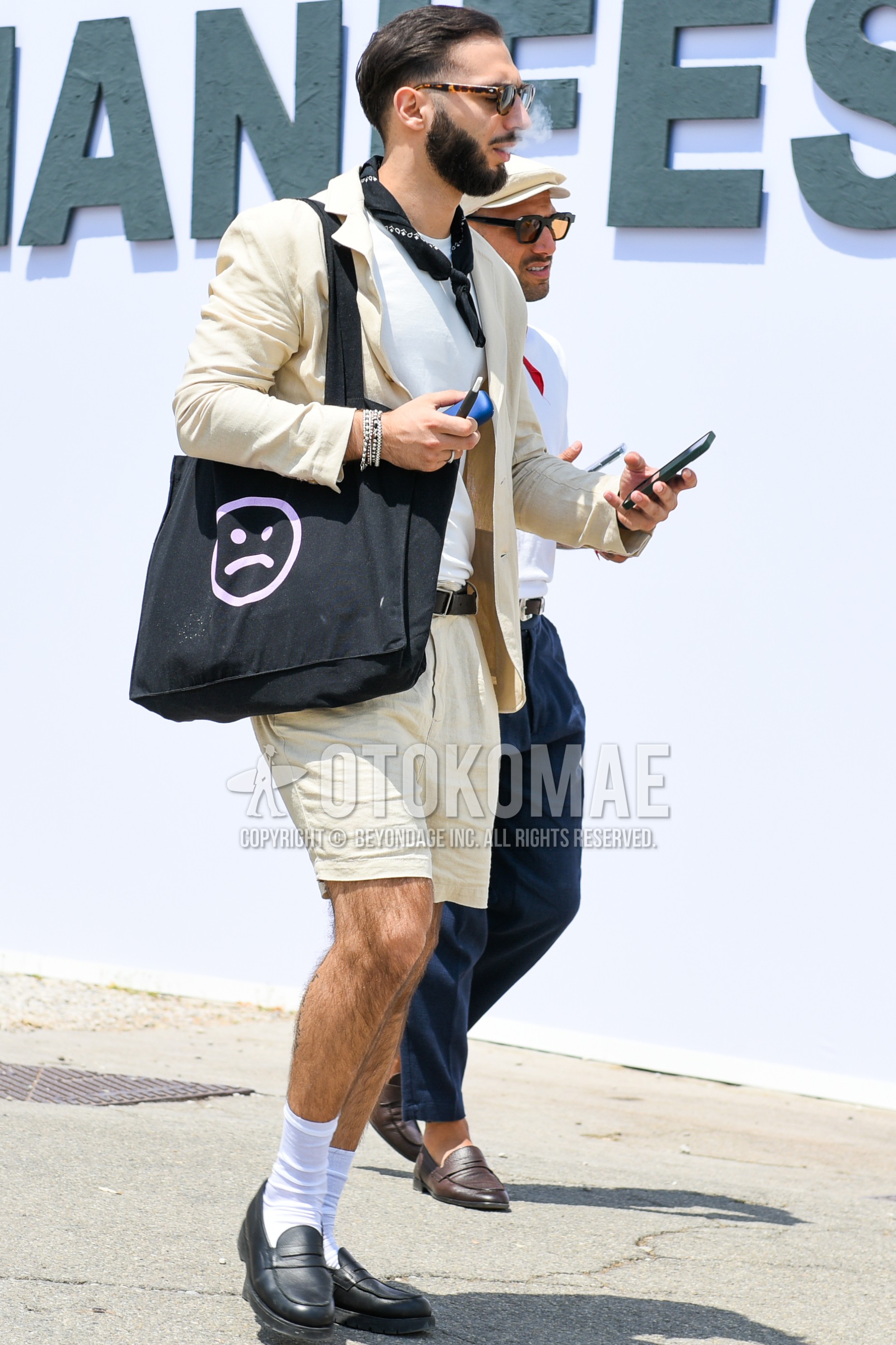 Men's spring summer outfit with black plain sunglasses, black scarf bandana/neckerchief, white plain t-shirt, white plain socks, black coin loafers leather shoes, black one point tote bag, beige plain casual setup.