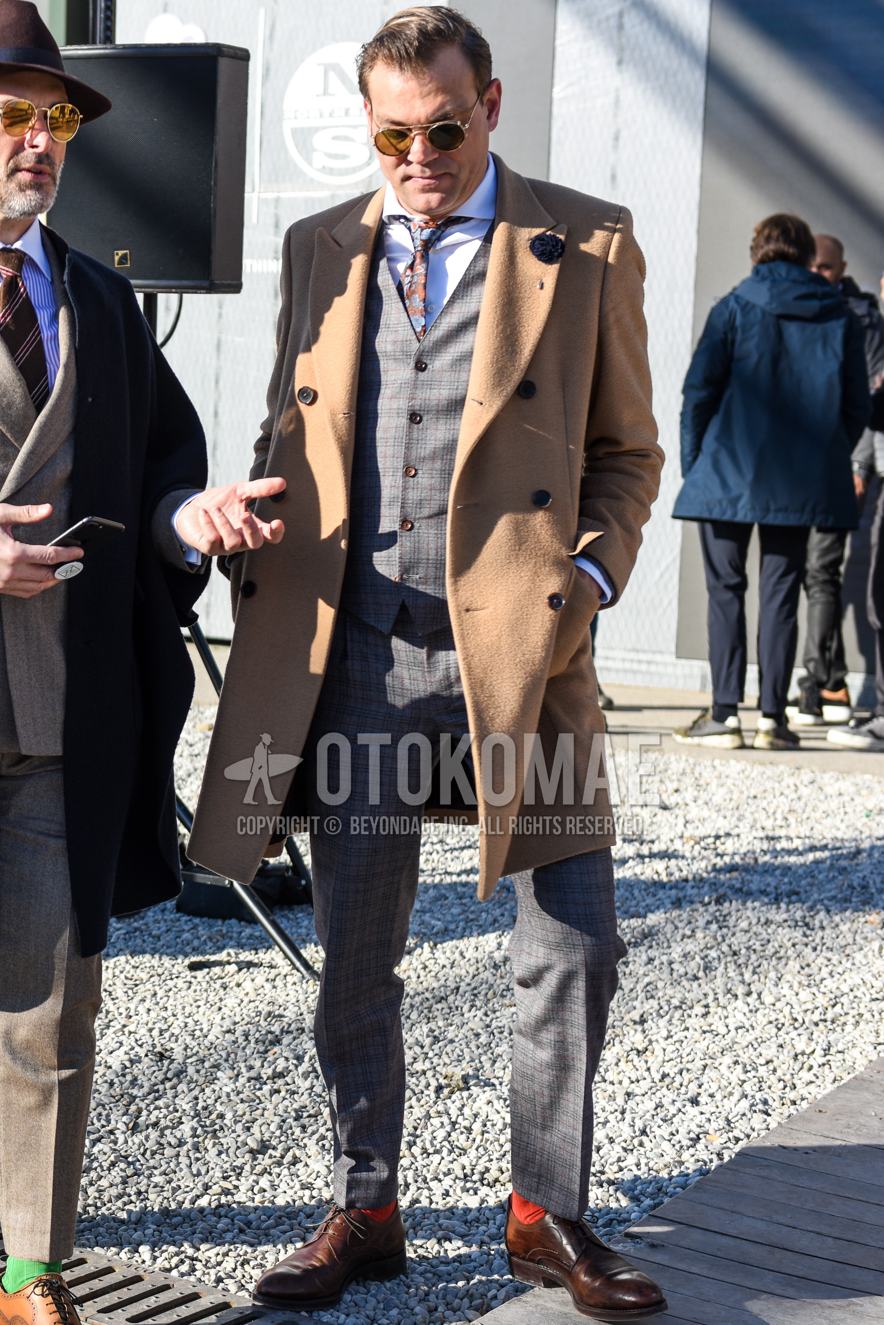 Men's autumn winter outfit with gold plain sunglasses, beige plain chester coat, white plain shirt, orange plain socks, brown plain toe leather shoes, multi-color necktie necktie.