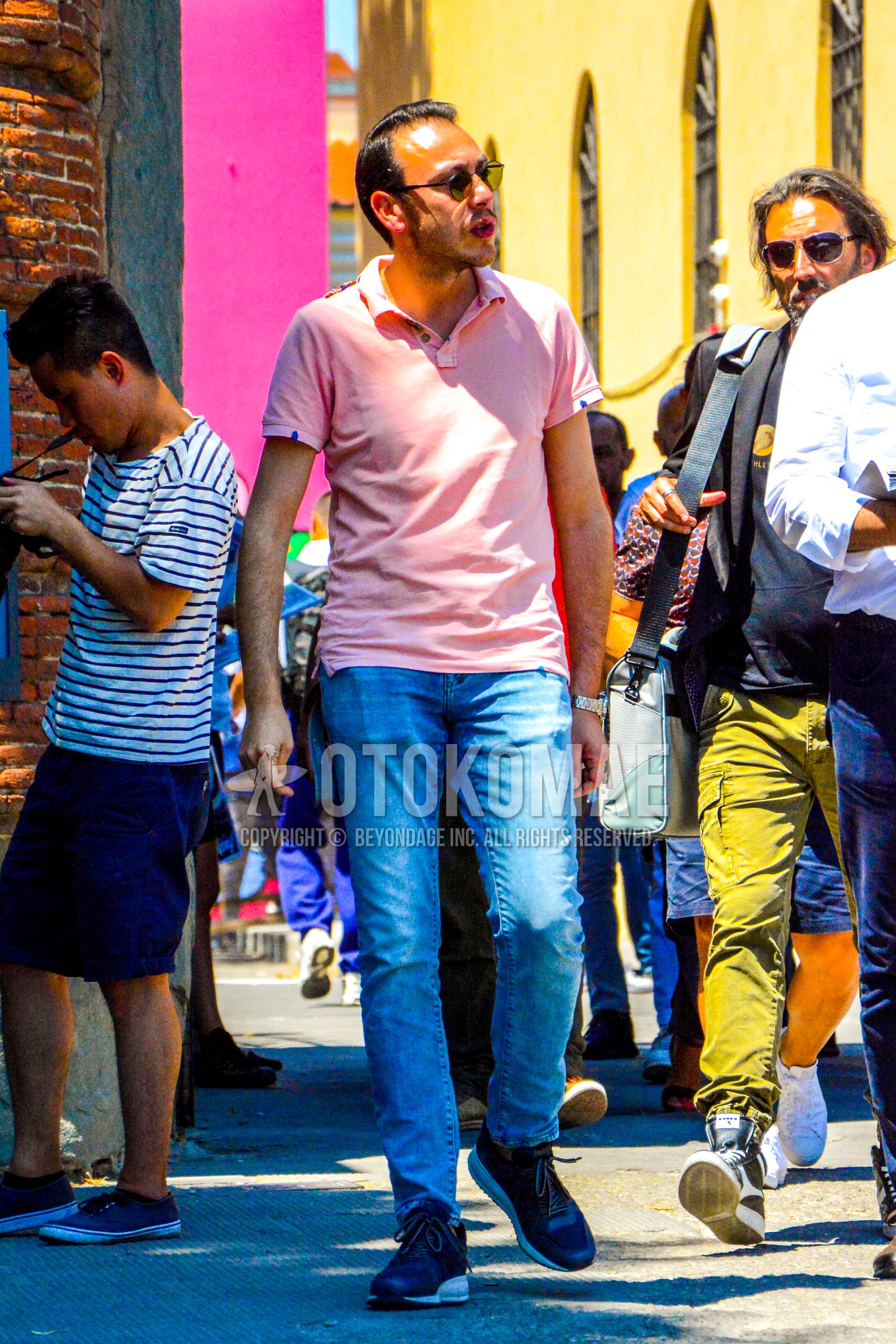 Men's summer outfit with plain sunglasses, pink plain polo shirt, blue plain denim/jeans, black high-cut sneakers.