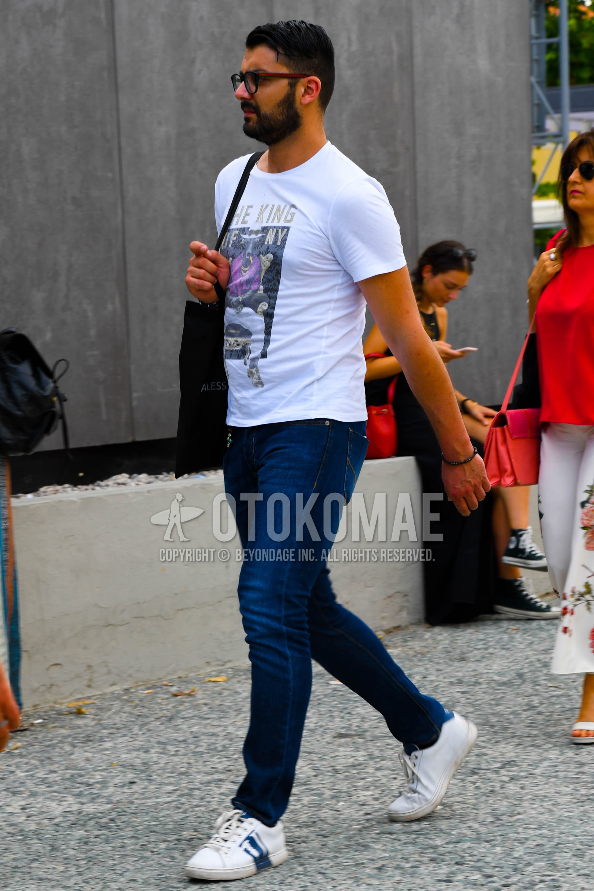 Men's summer outfit with plain glasses, white graphic t-shirt, blue plain denim/jeans, white low-cut sneakers.