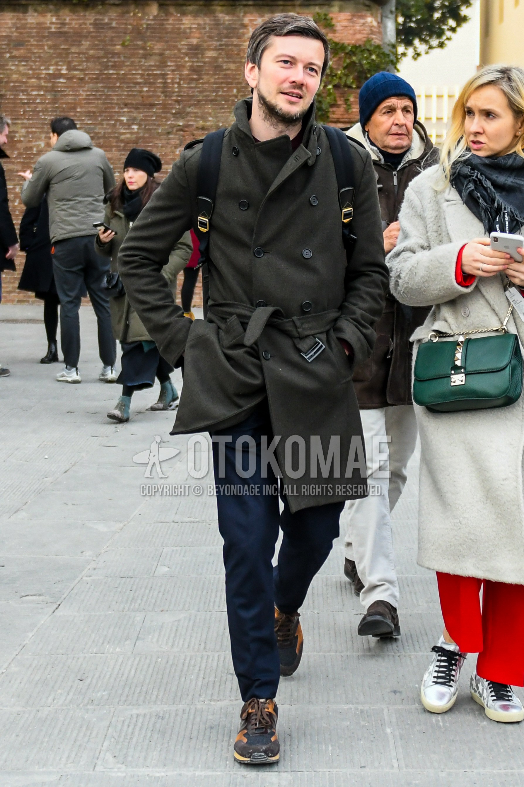 Men's winter outfit with olive green plain trench coat, navy plain slacks, black orange low-cut sneakers.