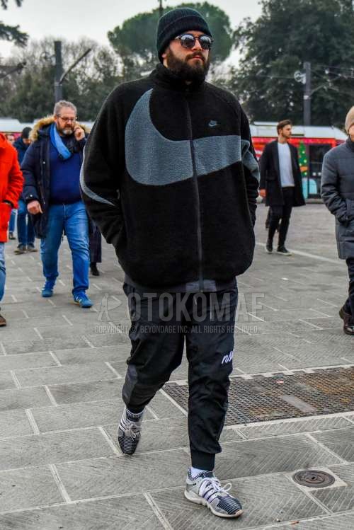 黒無地のニットキャップ、無地のサングラス、ナイキの黒無地のフリースジャケット、ナイキの黒デカロゴのジョガーパンツ/リブパンツ、白無地のソックス、アディダスの白ローカットのスニーカーを合わせた冬のメンズコーデ・着こなし。