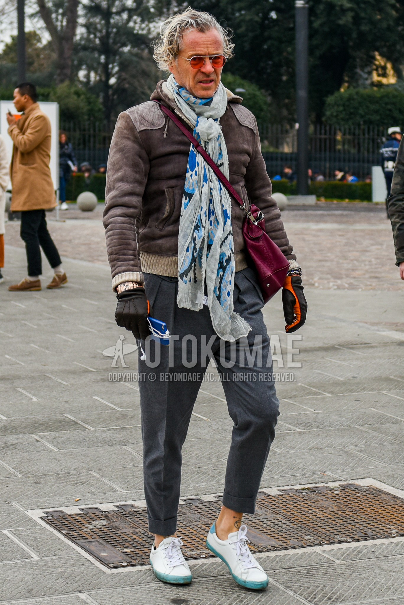 Men's winter outfit with plain sunglasses, white scarf scarf, brown plain outerwear, gray plain pleated pants, gray plain slacks, white sneakers, red plain shoulder bag.