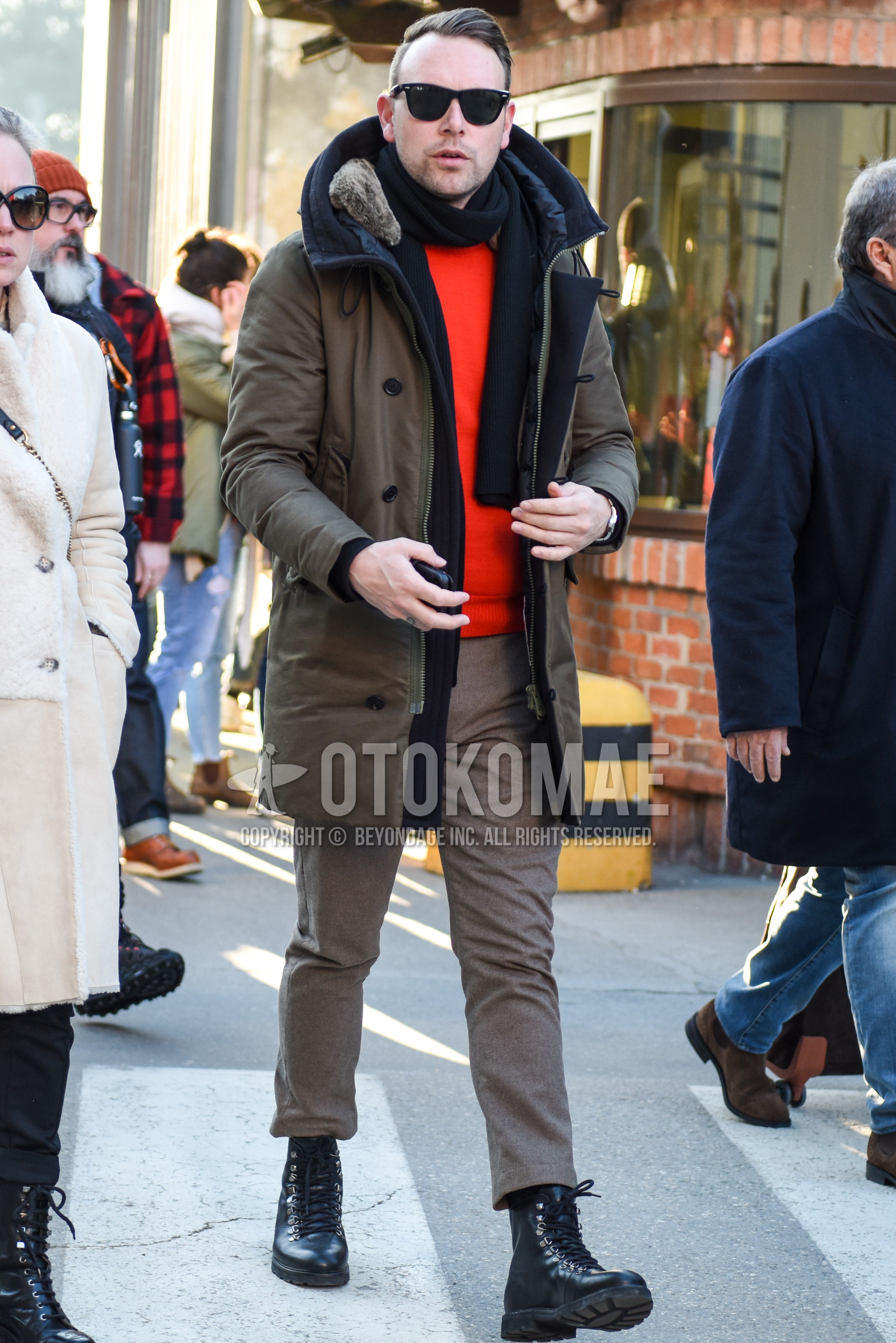 Men's winter outfit with black plain sunglasses, navy plain scarf, beige plain down jacket, orange plain sweater, brown plain slacks, black  boots.