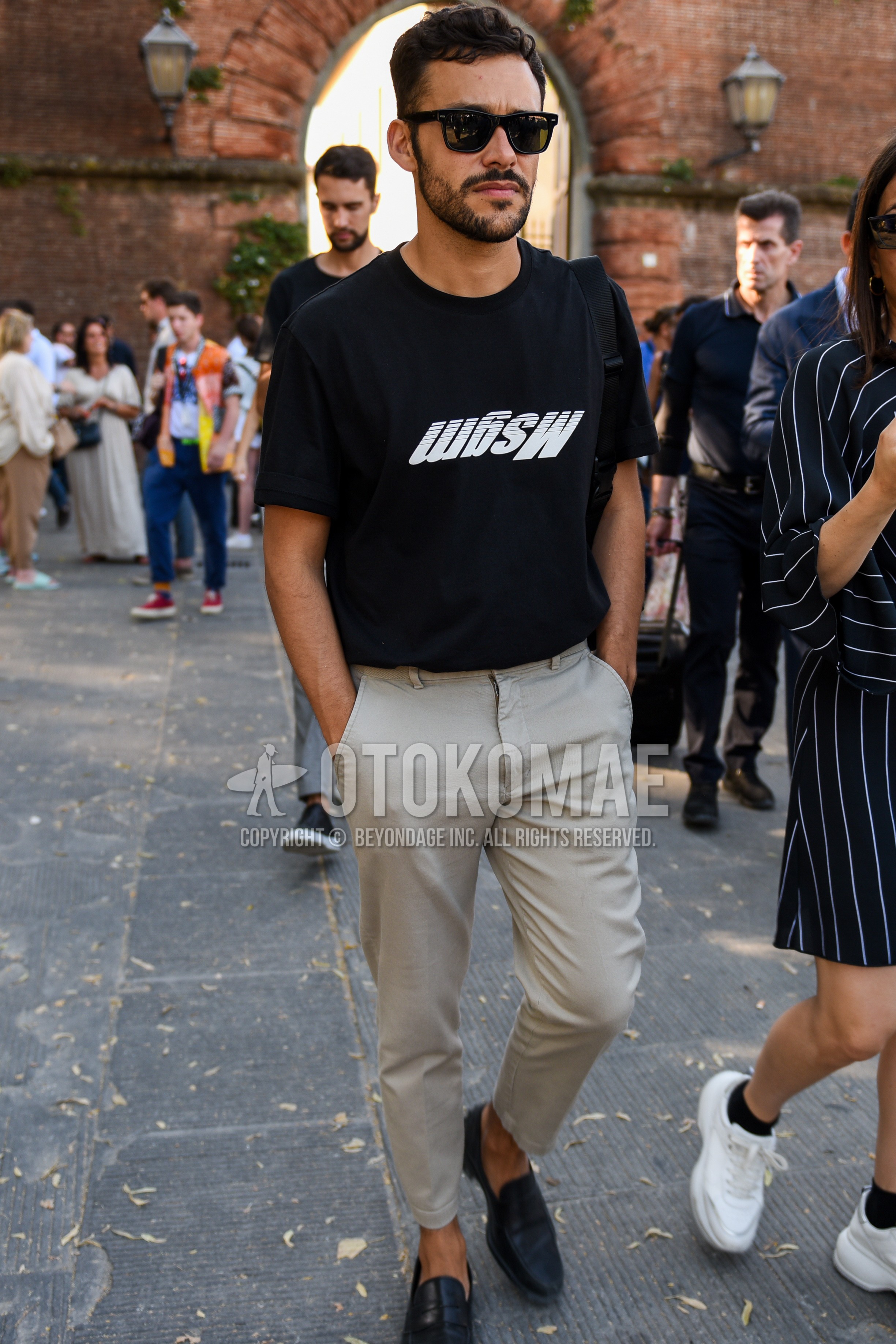 Men's summer outfit with black plain sunglasses, black graphic t-shirt, beige plain chinos, black coin loafers leather shoes.