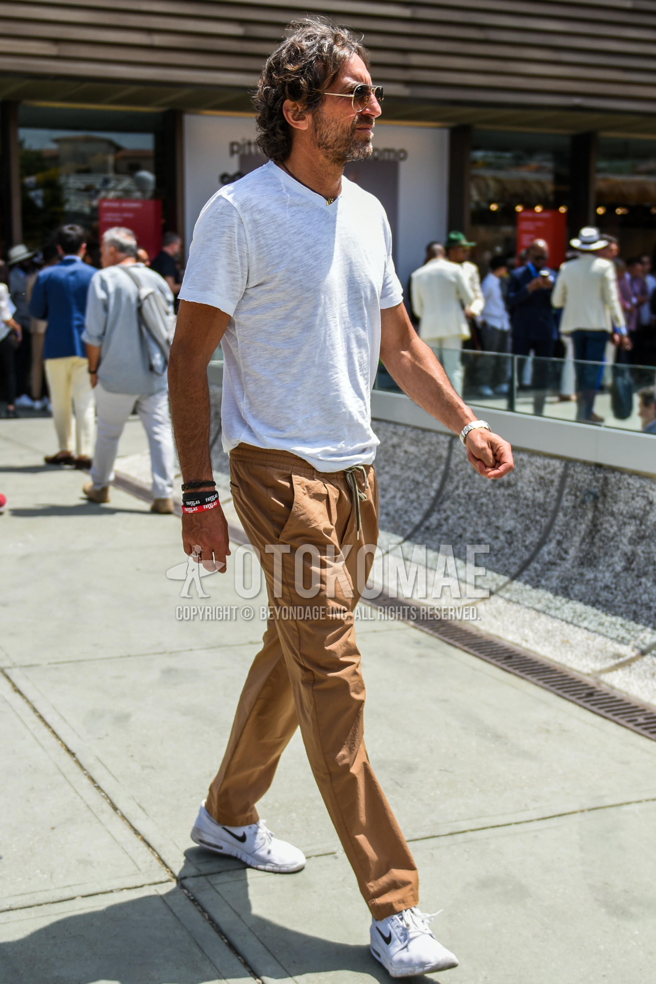 Men's summer outfit with gold plain sunglasses, white plain t-shirt, brown plain easy pants, white low-cut sneakers.