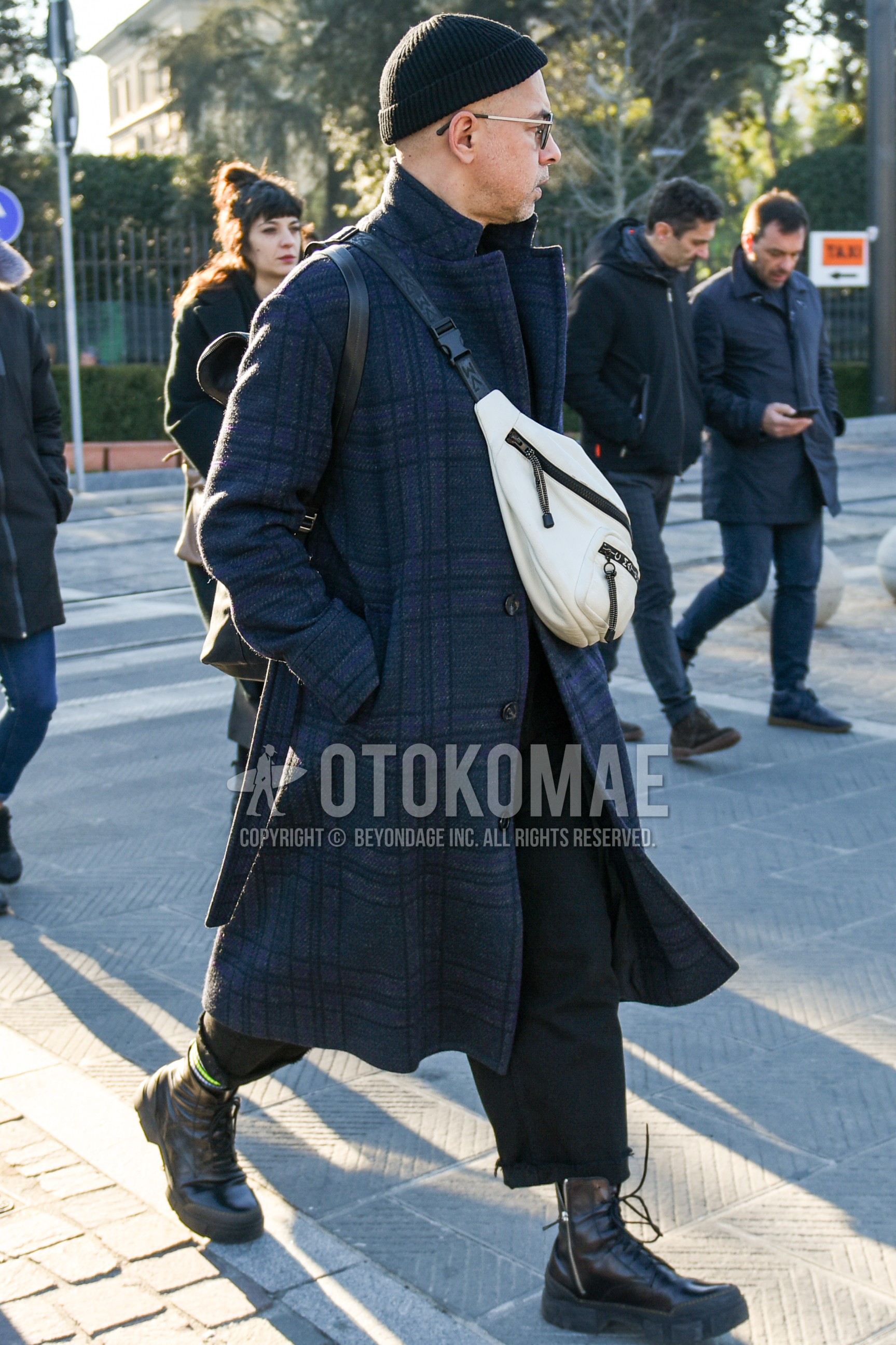Men's autumn winter outfit with black plain knit cap, black plain glasses, gray check chester coat, dark gray plain slacks, brown  boots, white plain shoulder bag.