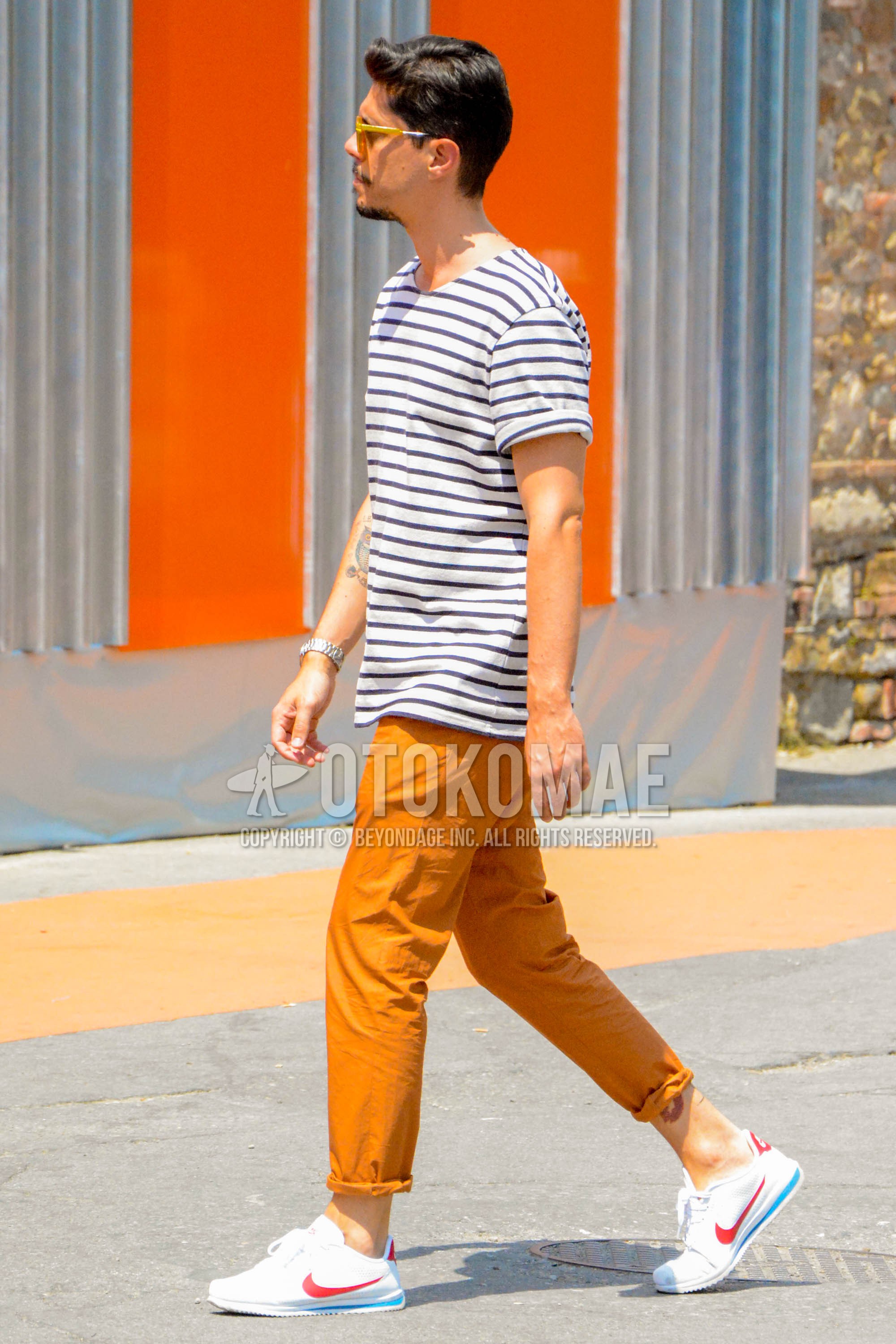 Men's summer outfit with white horizontal stripes t-shirt, orange plain cotton pants, white low-cut sneakers.
