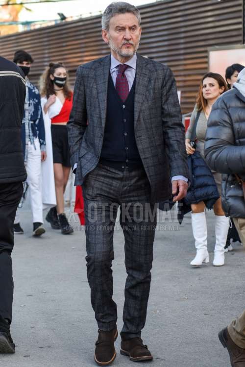 白トップス/インナーのシャツ、ネイビー無地のカーディガン、スエードのブラウンモンクシューズの革靴、グレーチェックのスーツ、レッドネクタイのネクタイを合わせた春秋のメンズコーデ・着こなし。