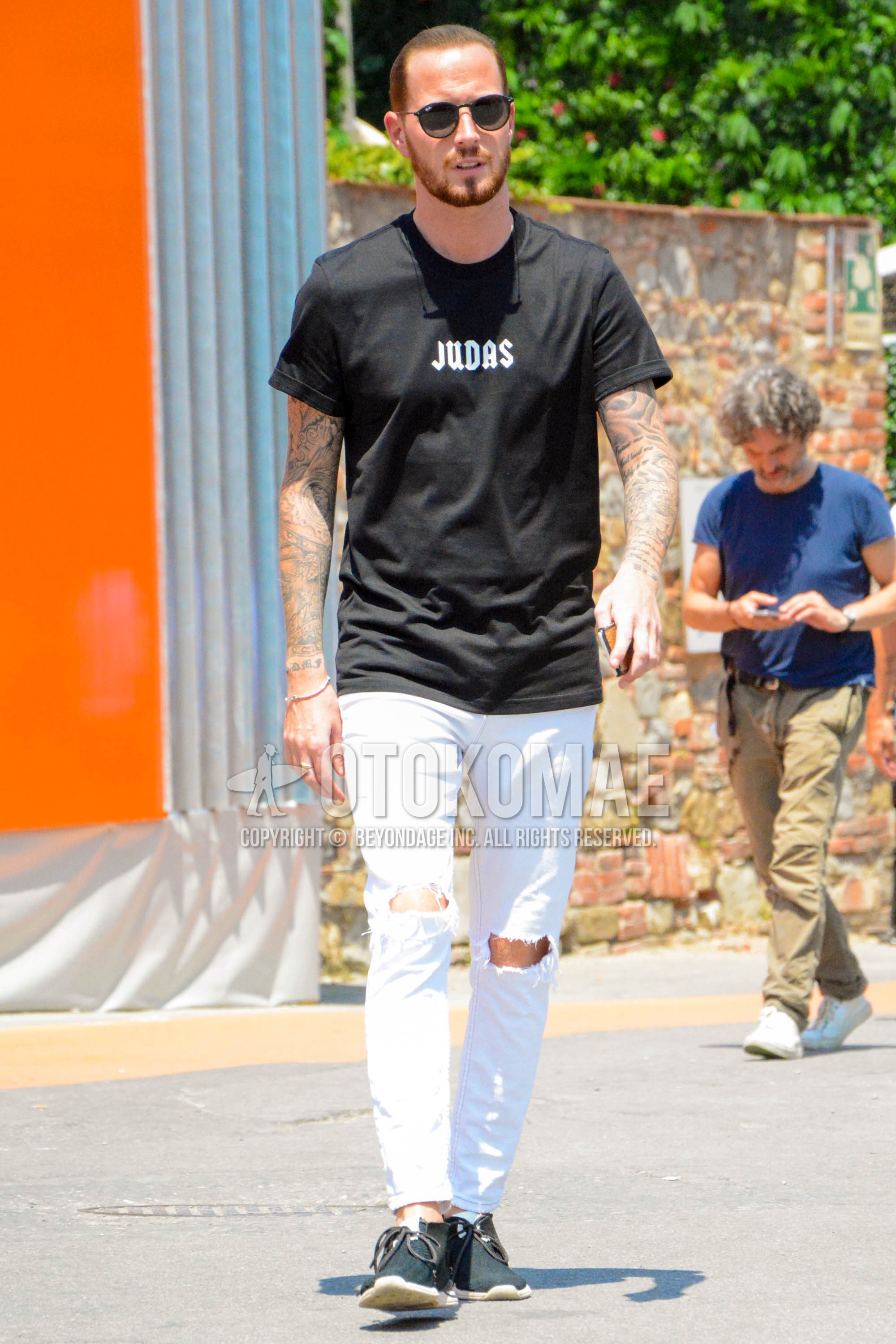 Men's summer outfit with plain sunglasses, black graphic t-shirt, white plain damaged jeans, black low-cut sneakers.