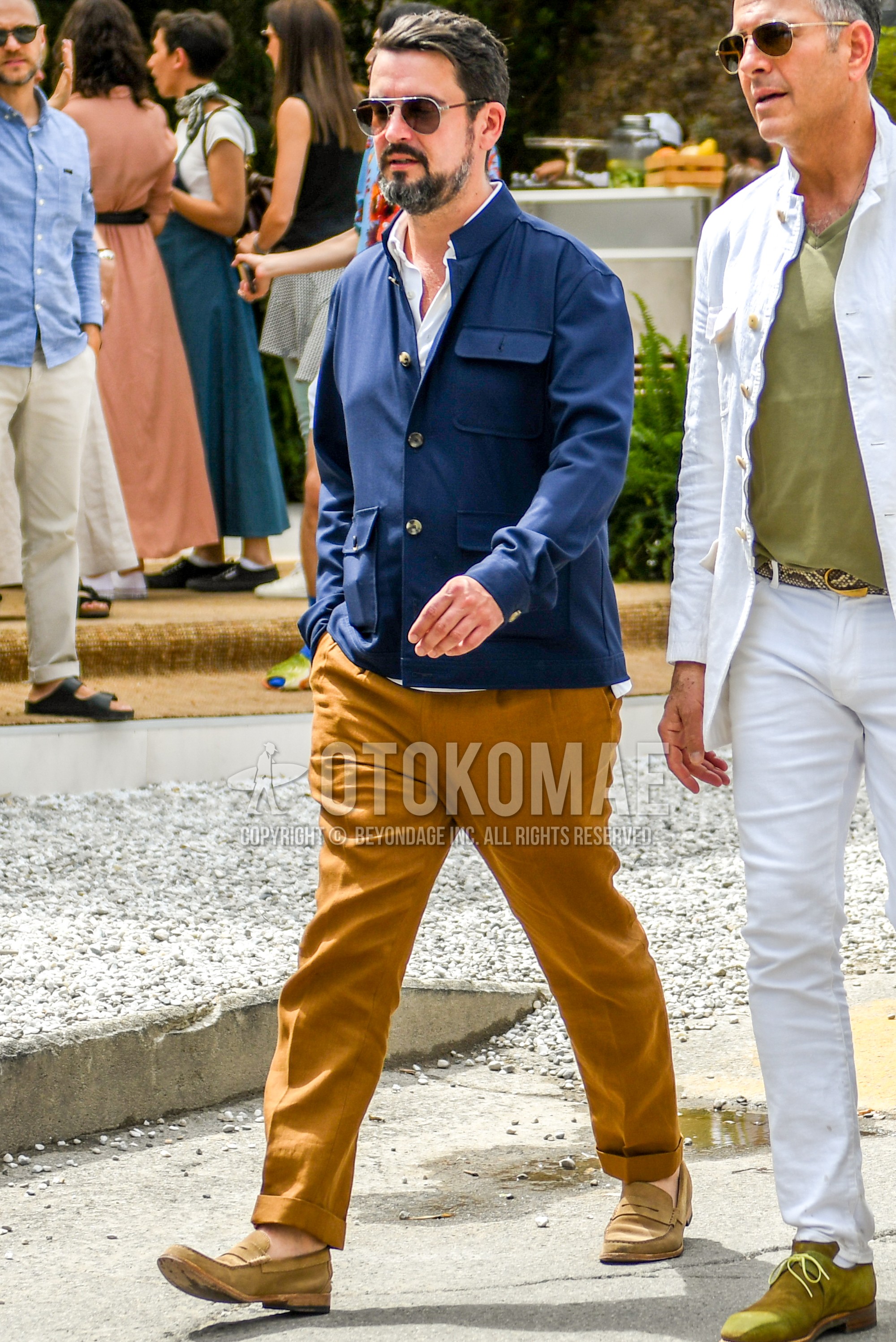 Men's spring summer autumn outfit with plain sunglasses, navy plain outerwear, white plain shirt, orange plain slacks, brown coin loafers leather shoes.