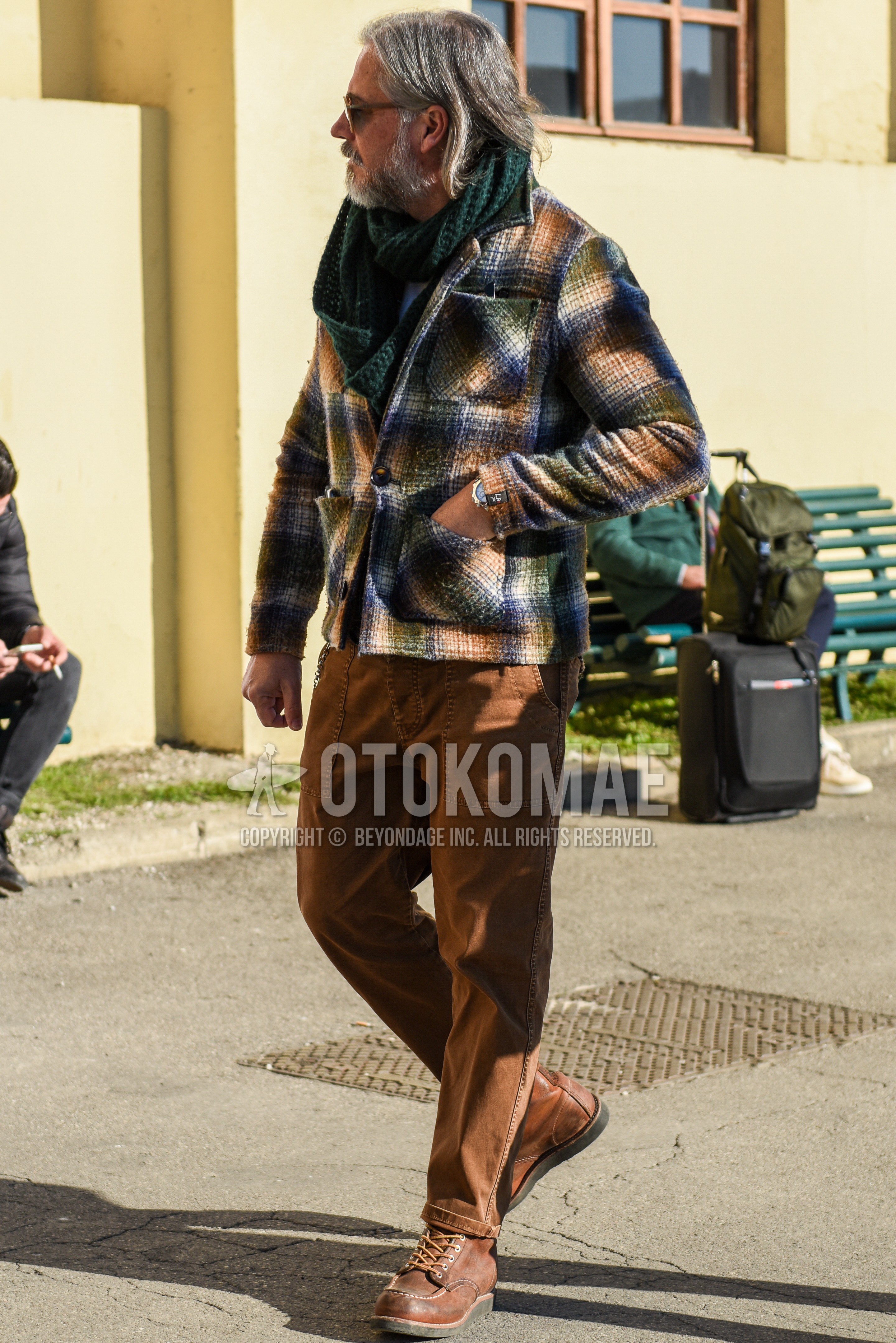 Men's autumn winter outfit with green plain scarf, multi-color check shirt jacket, brown plain chinos, brown work boots.
