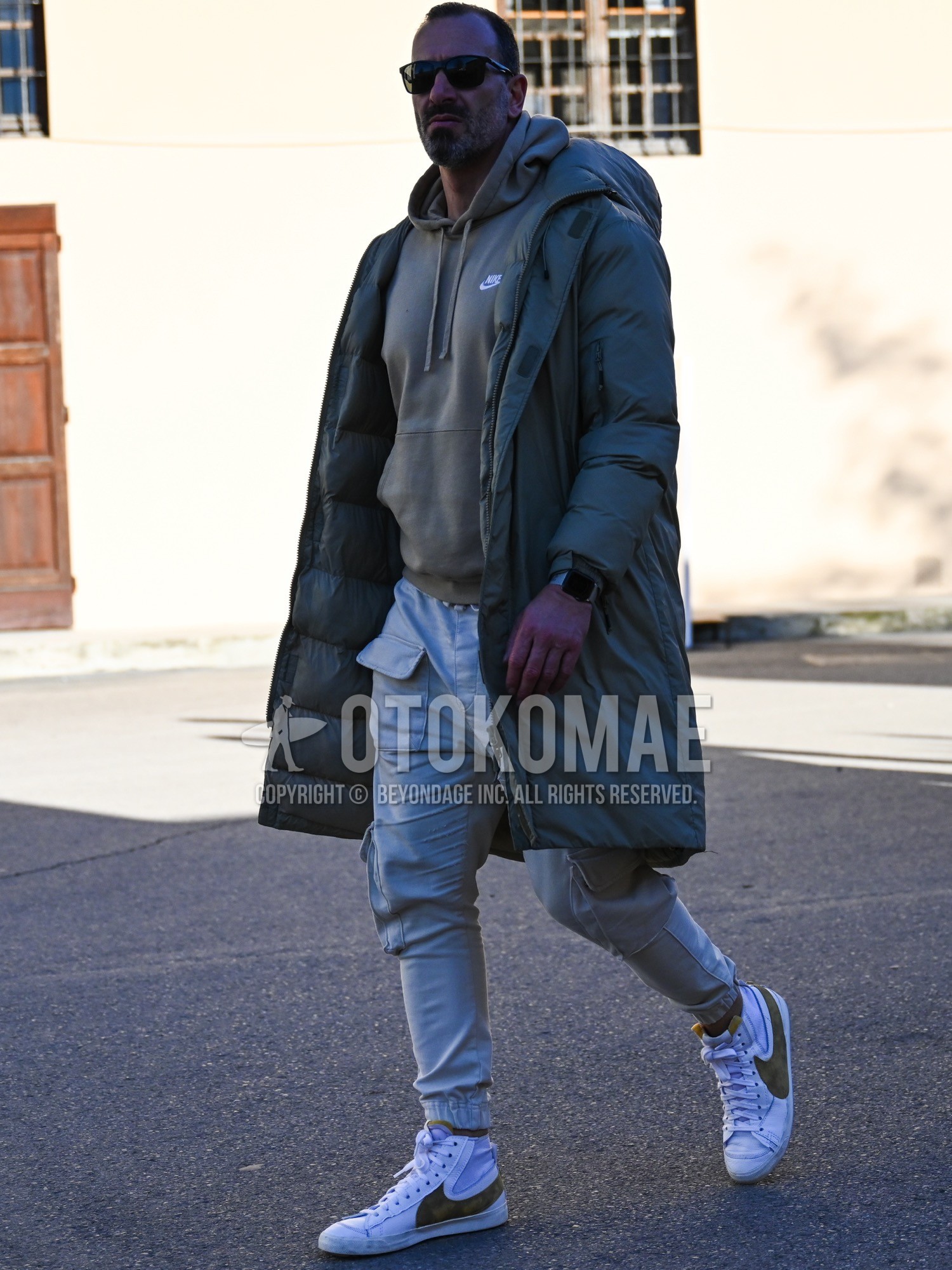 Men's autumn winter outfit with black plain sunglasses, olive green plain hooded coat, olive green plain down jacket, olive green one point hoodie, gray plain cargo pants, white olive green high-cut sneakers.