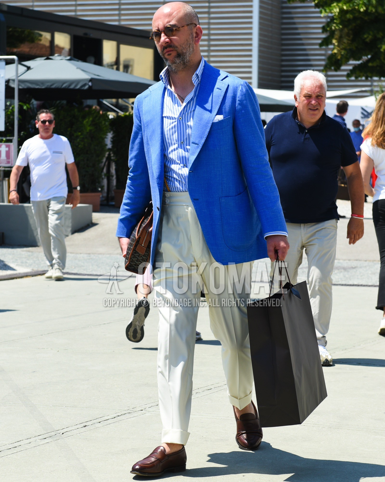 Men's spring summer outfit with brown tortoiseshell sunglasses, blue plain tailored jacket, blue stripes shirt, white plain slacks, brown coin loafers leather shoes, dark gray bag clutch bag/second bag/drawstring bag.