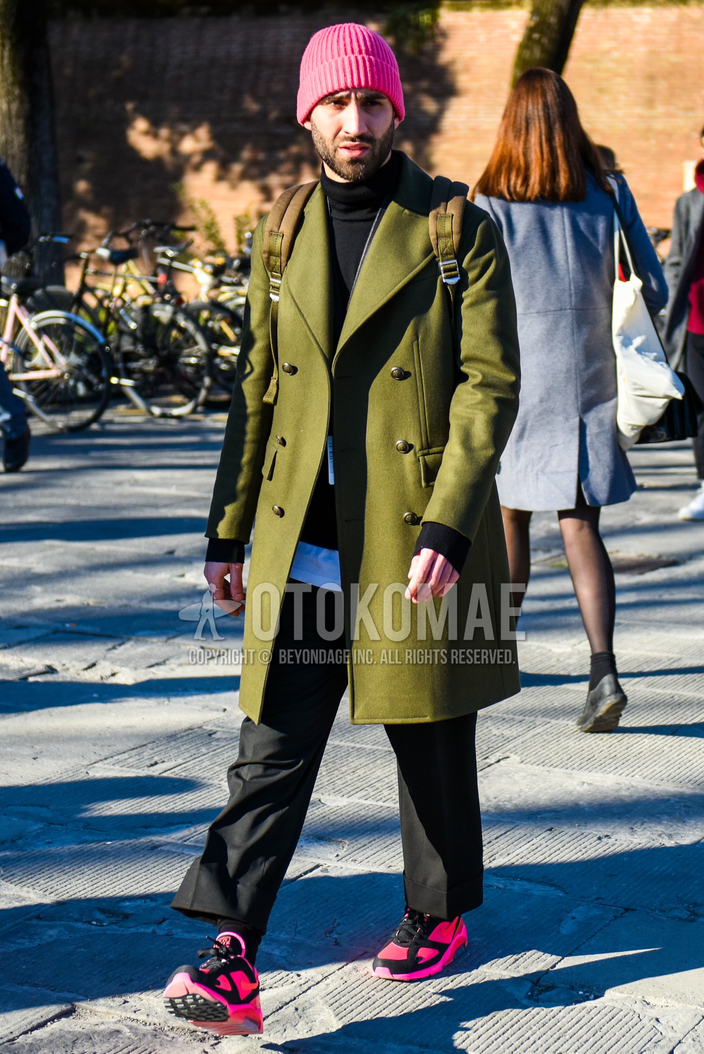 Men's autumn winter outfit with pink plain knit cap, olive green plain chester coat, black plain sweater, white plain t-shirt, black plain slacks, black plain socks, pink low-cut sneakers.