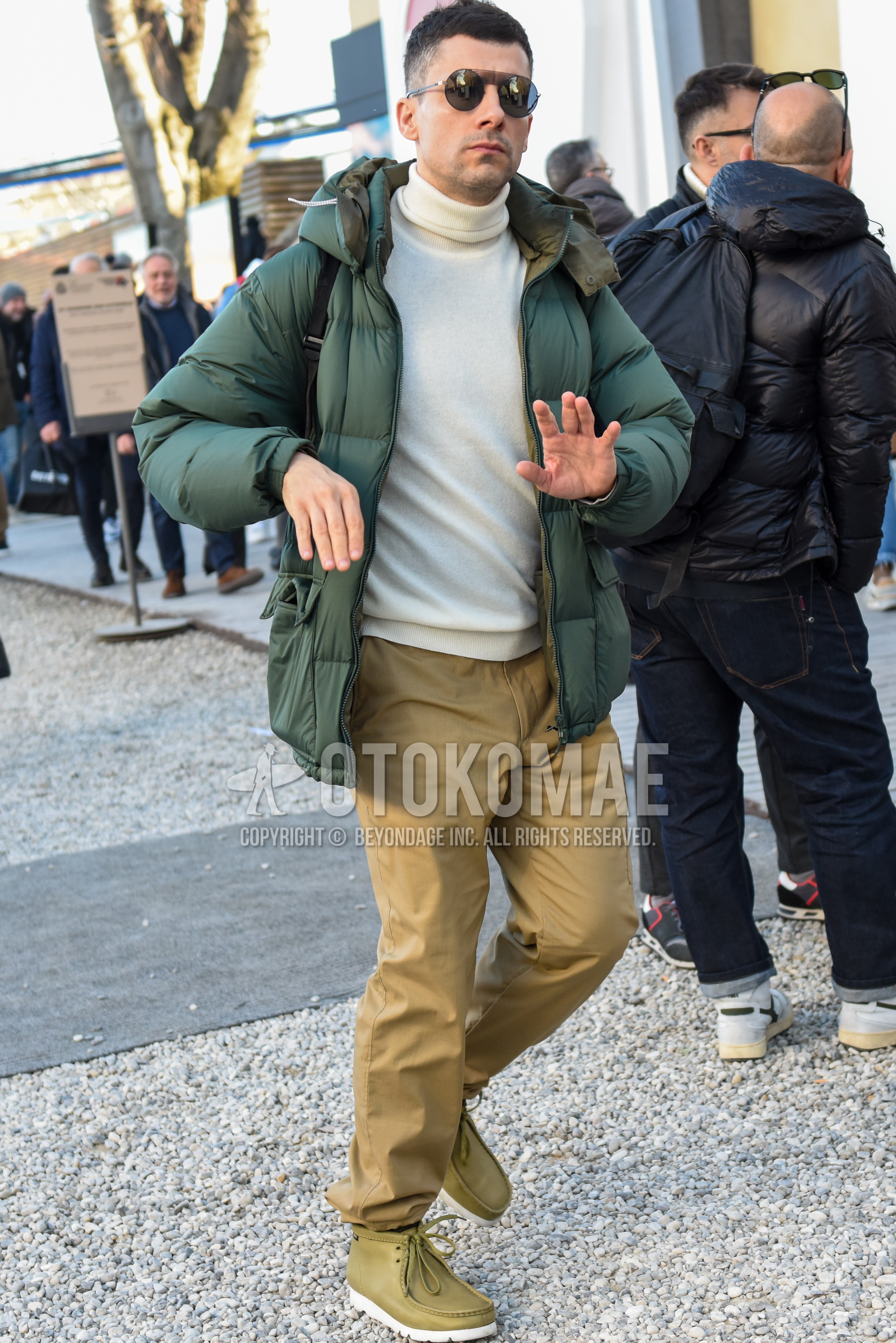Men's winter outfit with black plain sunglasses, olive green plain down jacket, white plain turtleneck knit, beige plain chinos, olive green high-cut sneakers.