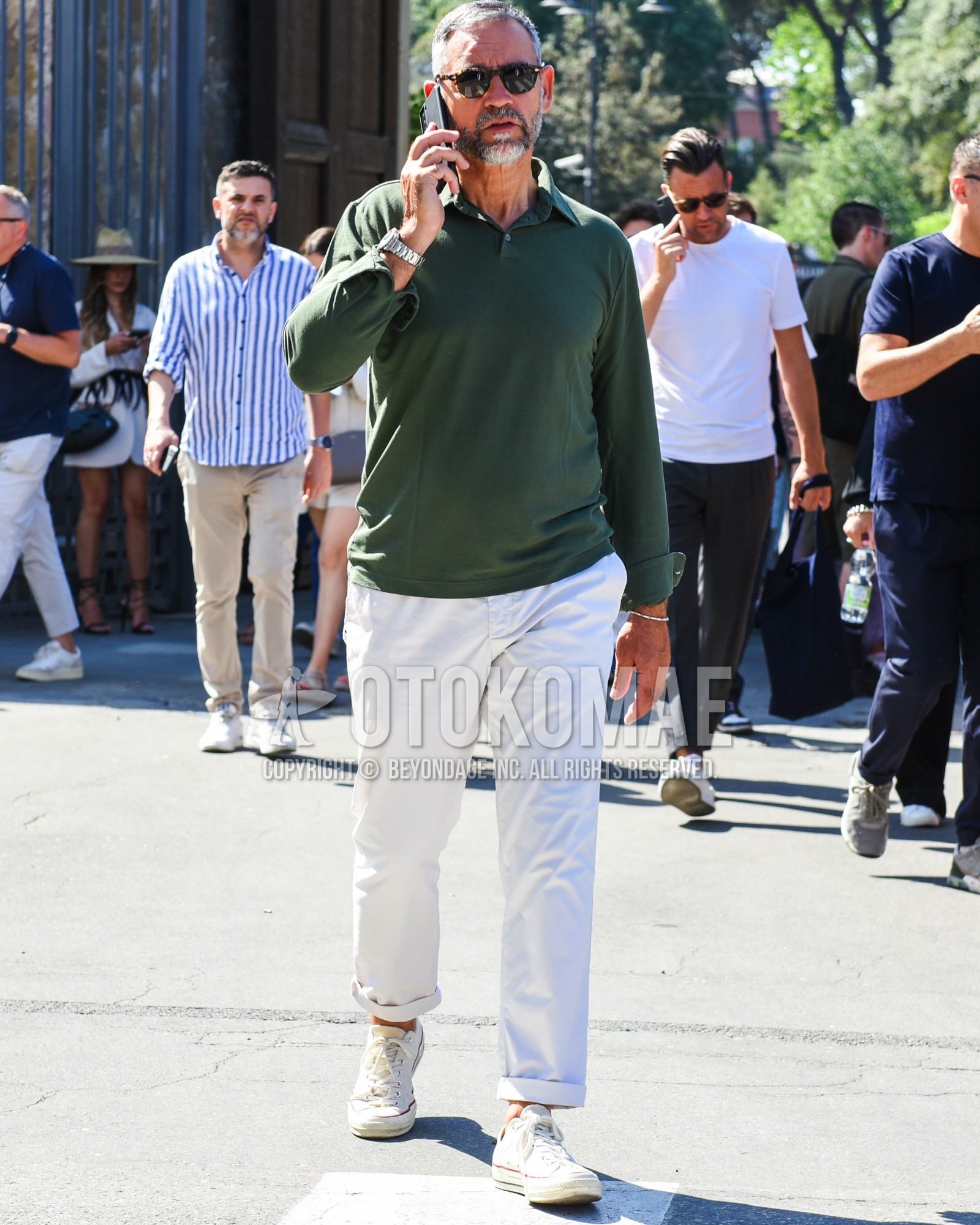 Men's spring summer outfit with brown tortoiseshell sunglasses, olive green plain polo shirt, white plain cotton pants, white low-cut sneakers.
