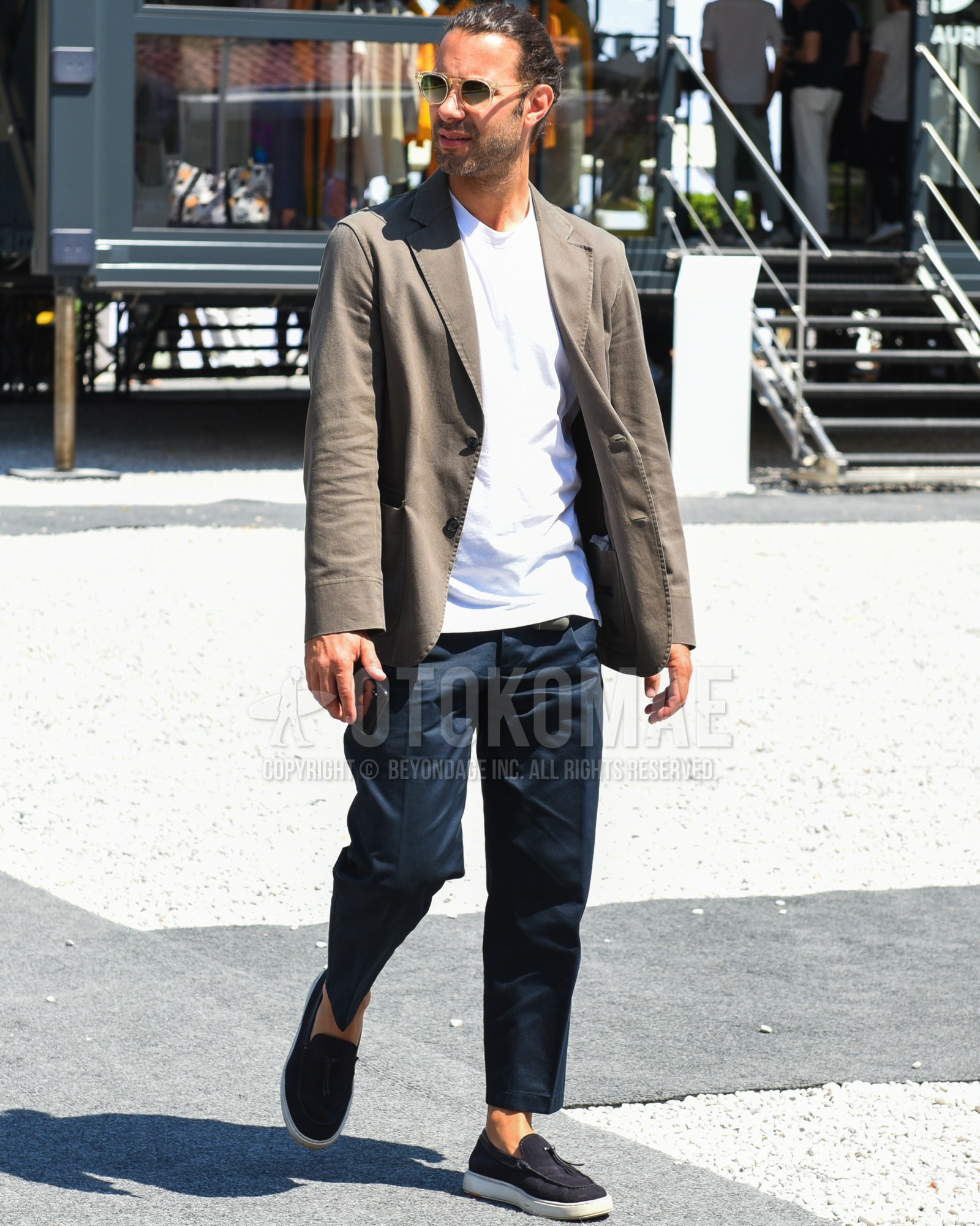 Men's spring summer outfit with clear plain sunglasses, brown plain  tailored jacket, white plain t-shirt, navy plain slacks, navy plain cropped  pants, black slip-on sneakers.