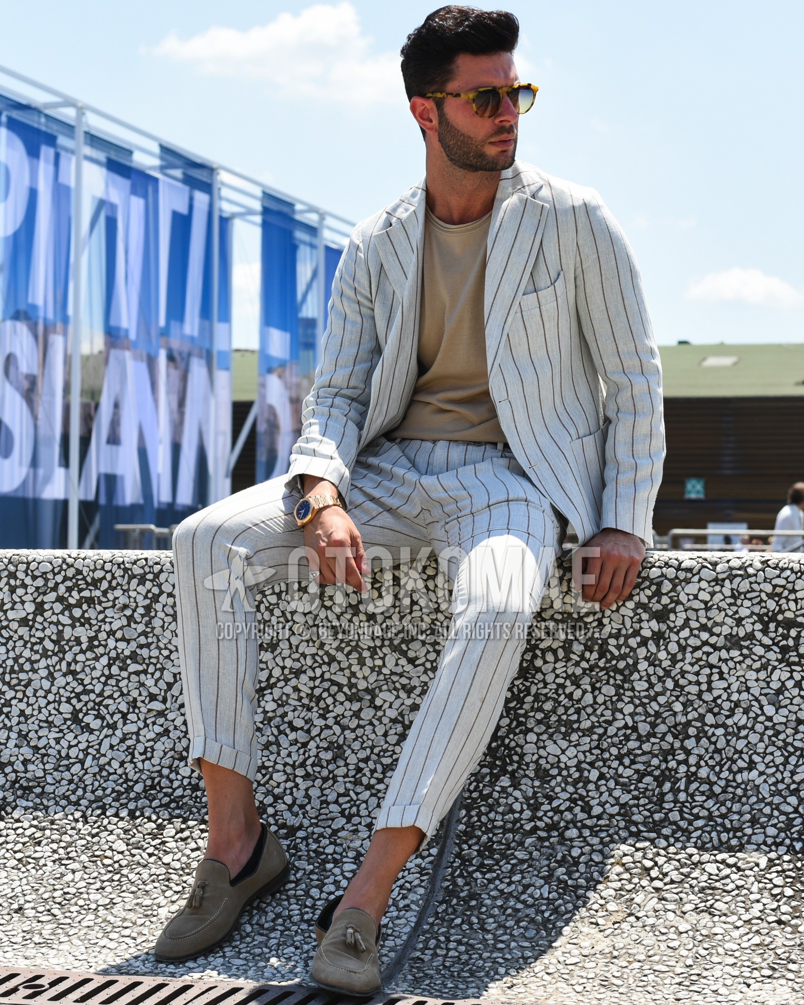Men's spring summer outfit with yellow tortoiseshell sunglasses, beige plain t-shirt, beige tassel loafers leather shoes, beige suede shoes leather shoes, white stripes suit.