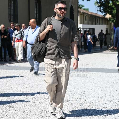 黒無地のサングラス、グレー無地のシャツ、グレー無地のTシャツ、ベージュ無地のチノパン、ベージュ無地のプリーツパンツ、白ローカットのスニーカー、グレー無地のバックパックを合わせた夏春のメンズコーデ・着こなし。