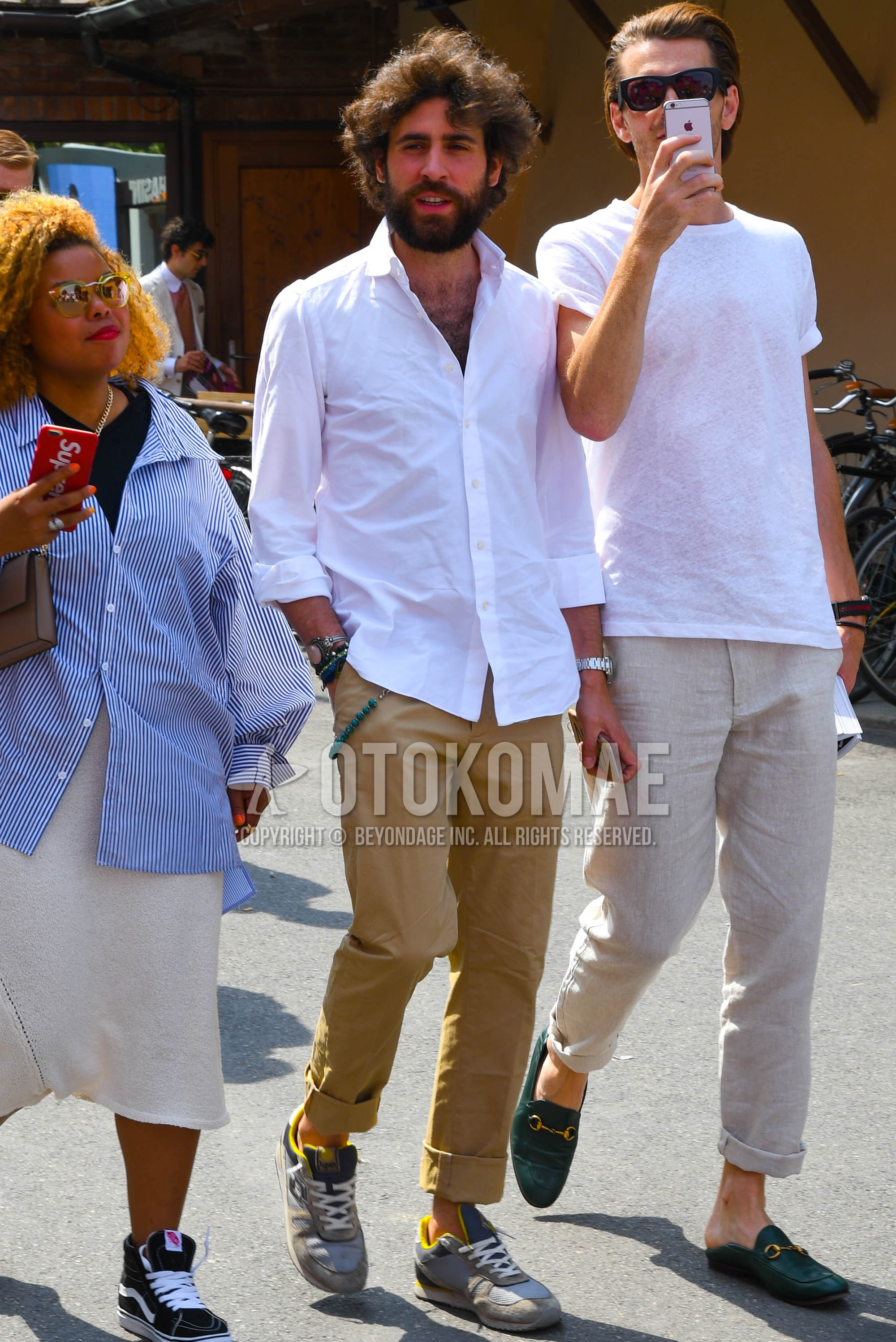 Men's spring summer outfit with white plain shirt, beige plain chinos, gray low-cut sneakers.
