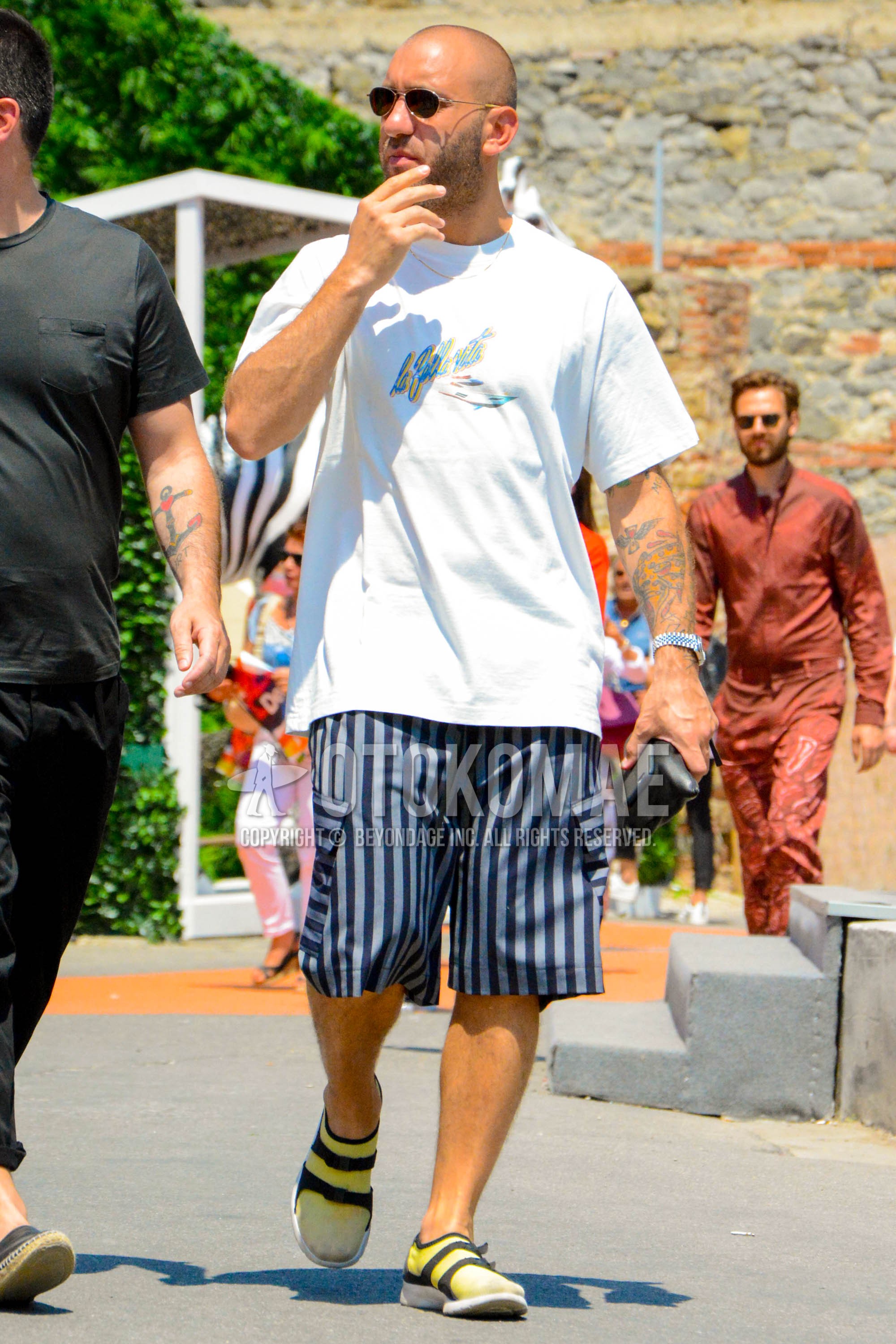 Men's summer outfit with white graphic t-shirt, blue stripes short pants, yellow plain socks, black sport sandals.