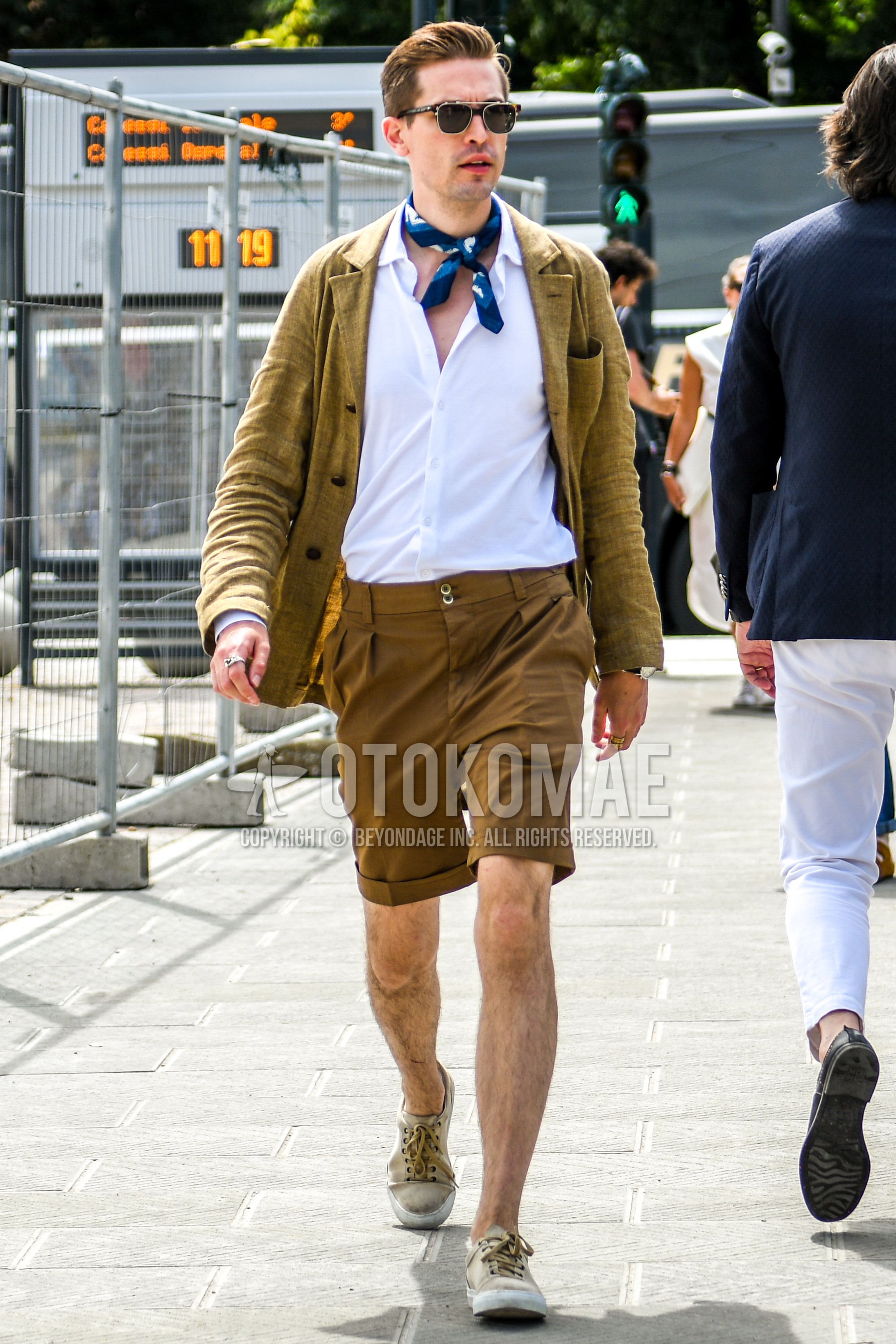 Men's spring summer outfit with brown tortoiseshell sunglasses, blue scarf bandana/neckerchief, beige plain tailored jacket, white plain shirt, brown plain short pants, brown plain beltless pants, beige low-cut sneakers.