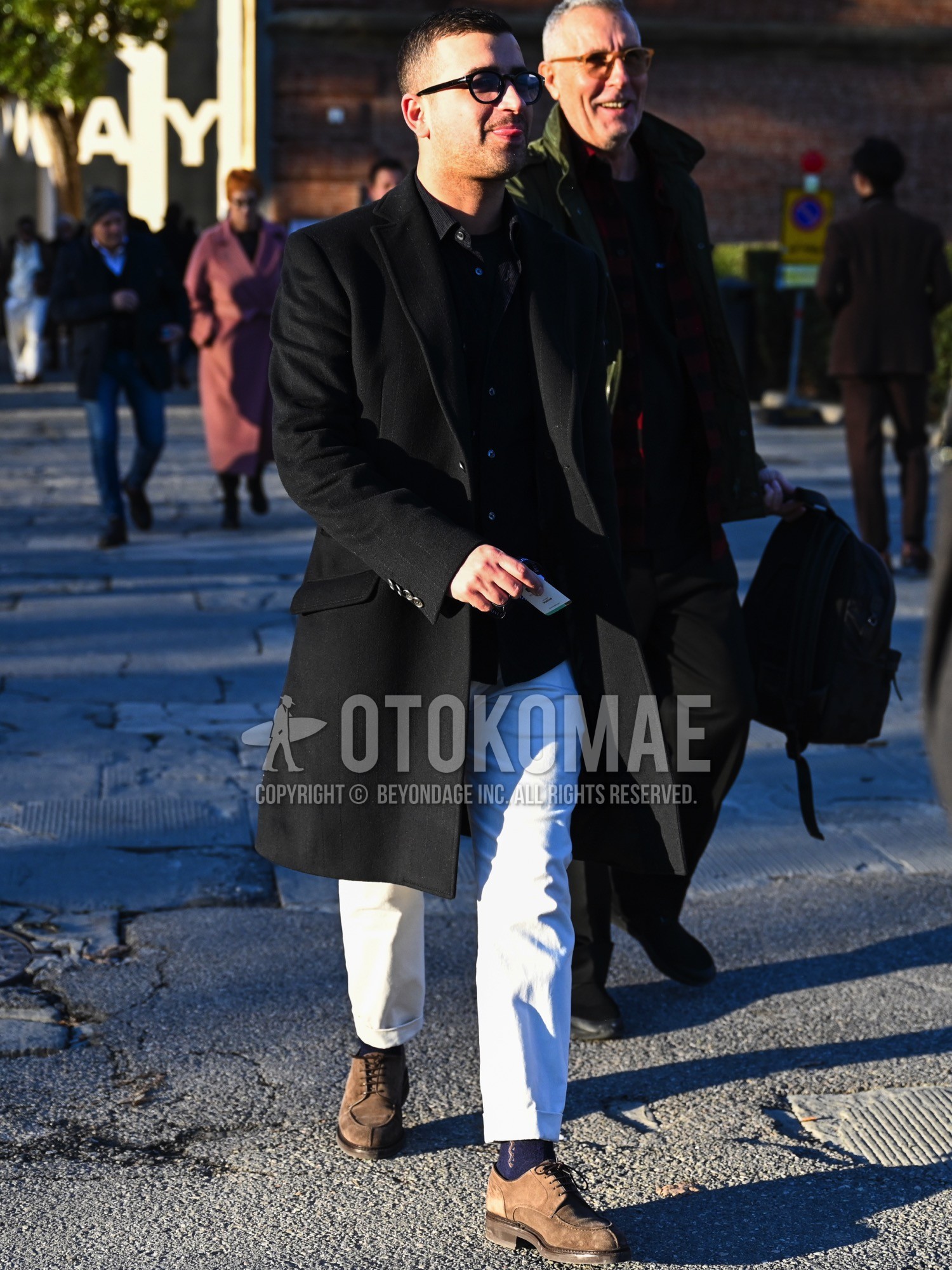 Men's autumn winter outfit with black plain glasses, black plain chester coat, black plain t-shirt, black plain shirt, white plain chinos, navy one point socks, brown u-tip shoes leather shoes, brown suede shoes leather shoes.