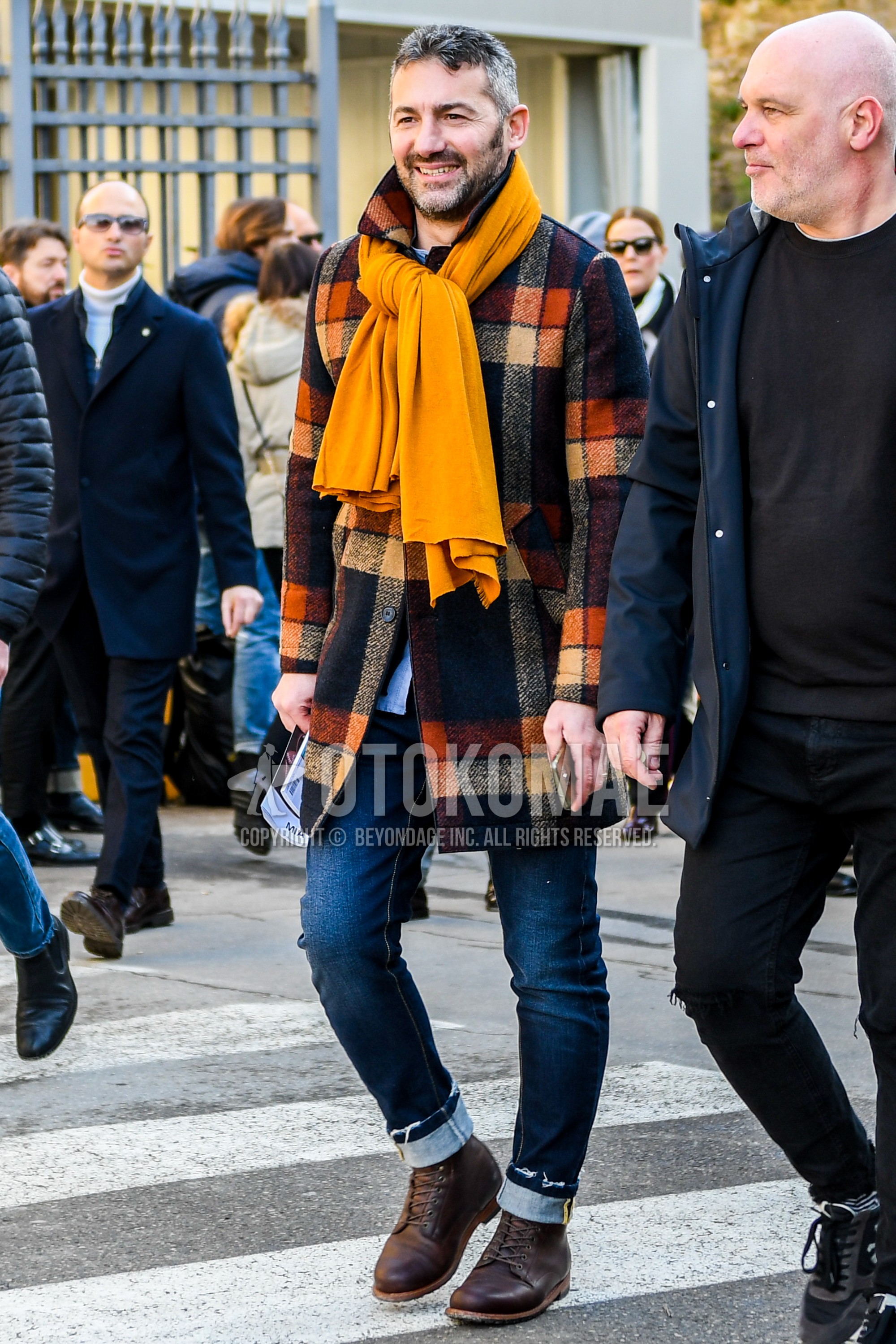 Men's autumn winter outfit with yellow plain scarf, multi-color check stenkarrer coat, blue plain denim/jeans, brown  boots.
