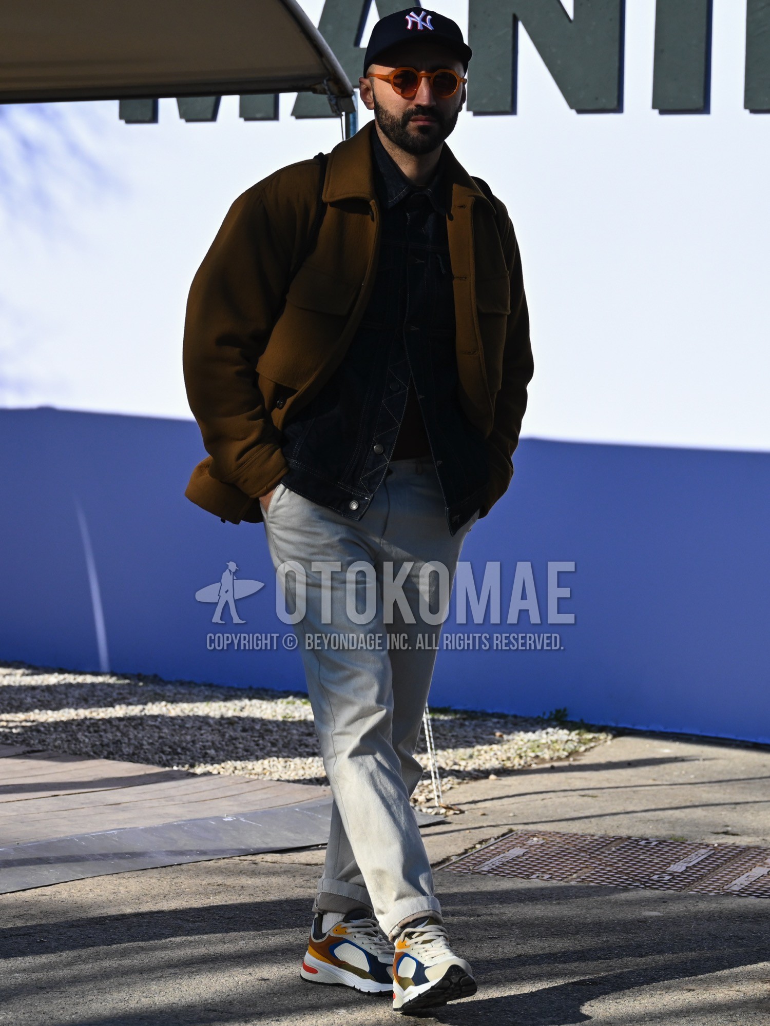 Men's autumn winter outfit with black one point baseball cap, brown plain sunglasses, brown plain coverall, black plain denim jacket, black plain long sleeve t-shirt, gray plain chinos, white plain socks, multi-color yellow navy olive green brown high-cut sneakers.