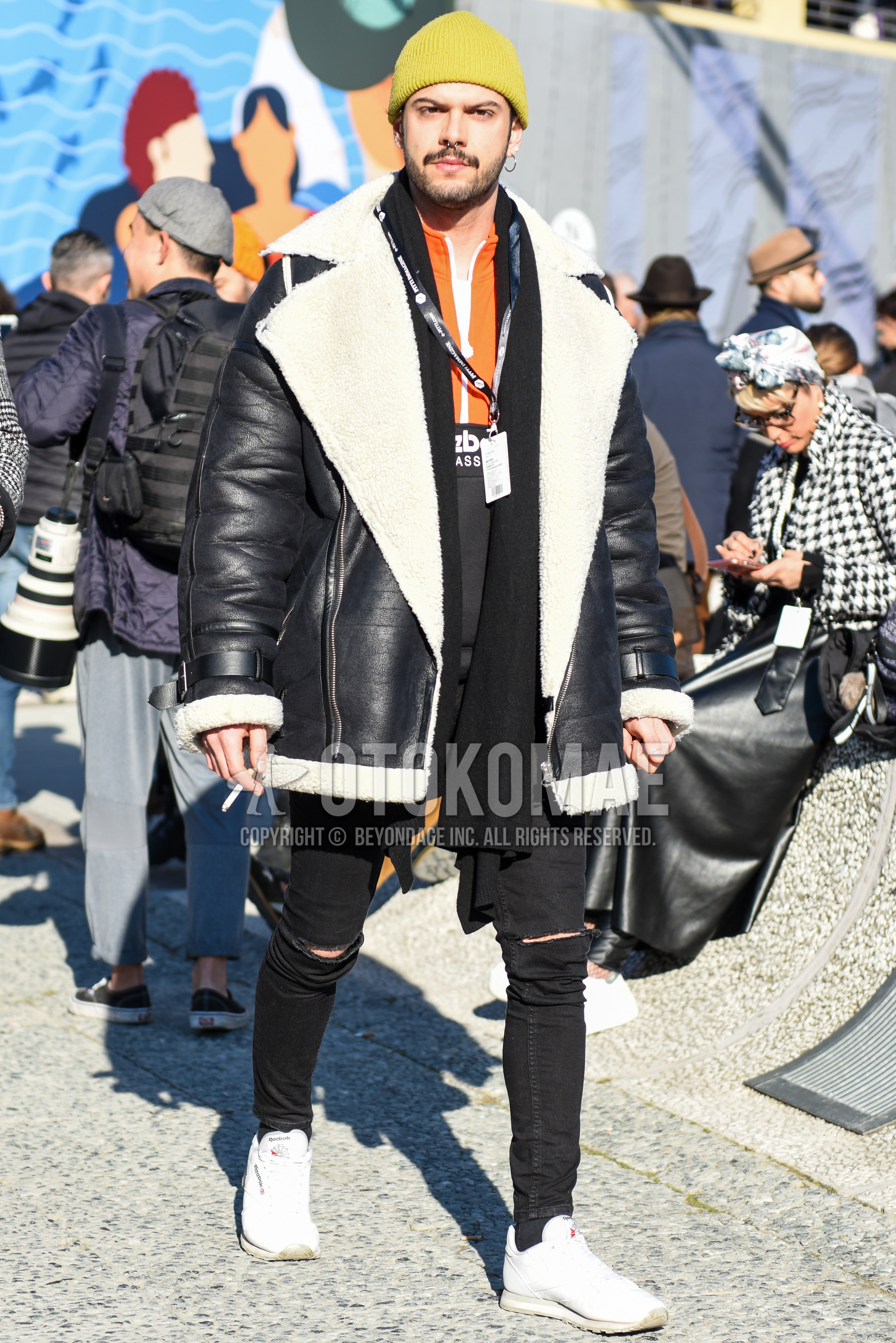 Men's winter outfit with yellow plain knit cap, black plain scarf, black plain leather jacket, orange black plain windbreaker, black plain damaged jeans, white low-cut sneakers.