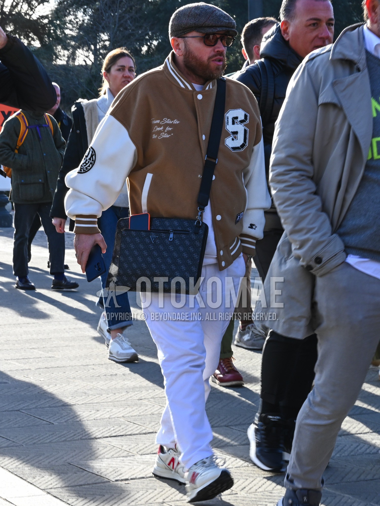 Men's autumn winter outfit with gray plain hunting cap, black plain sunglasses, brown plain stadium jacket, white plain sweatshirt, white plain cotton pants, white low-cut sneakers, black plain shoulder bag.