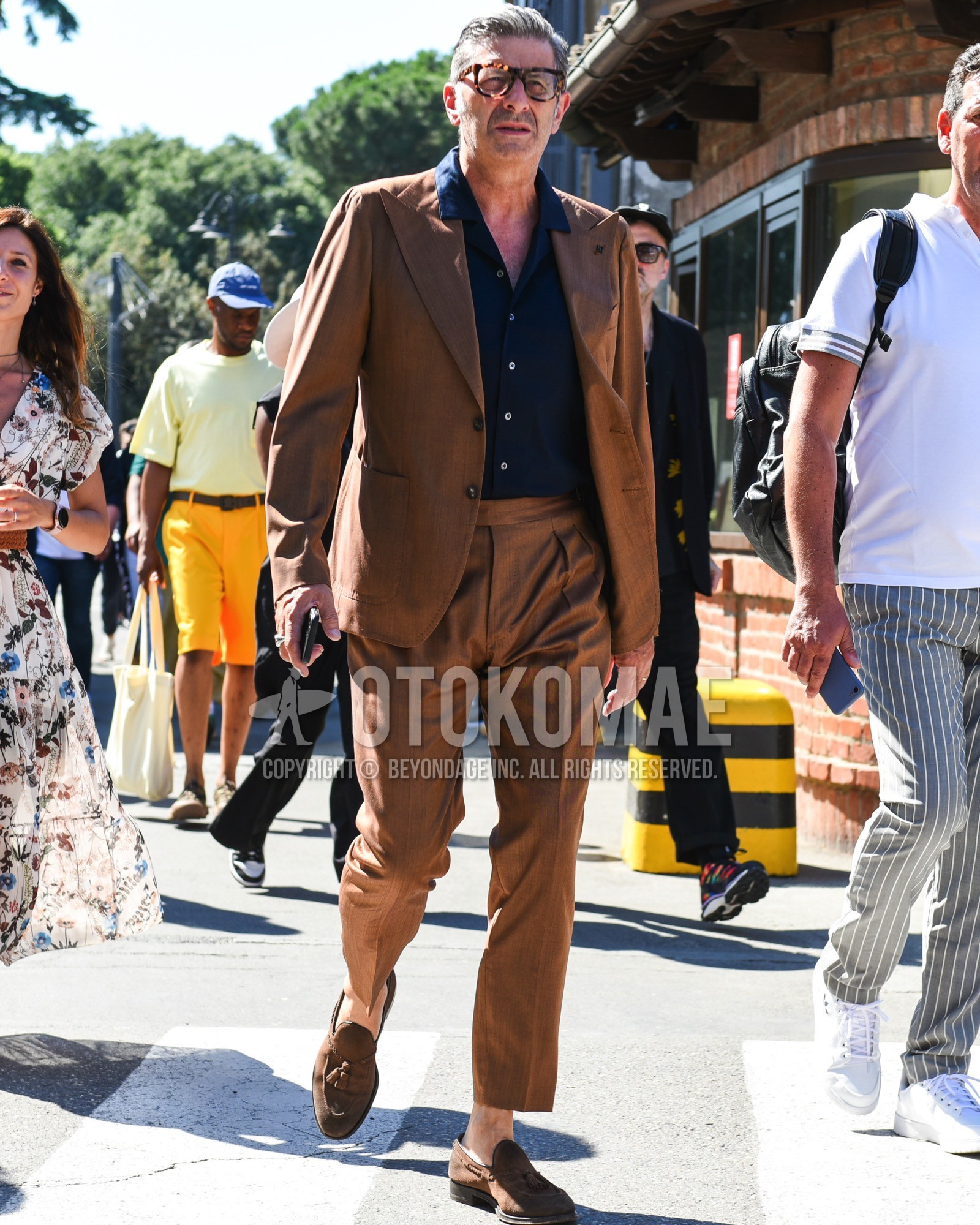 Men's spring summer outfit with brown tortoiseshell glasses, navy plain shirt, brown tassel loafers leather shoes, brown plain suit.