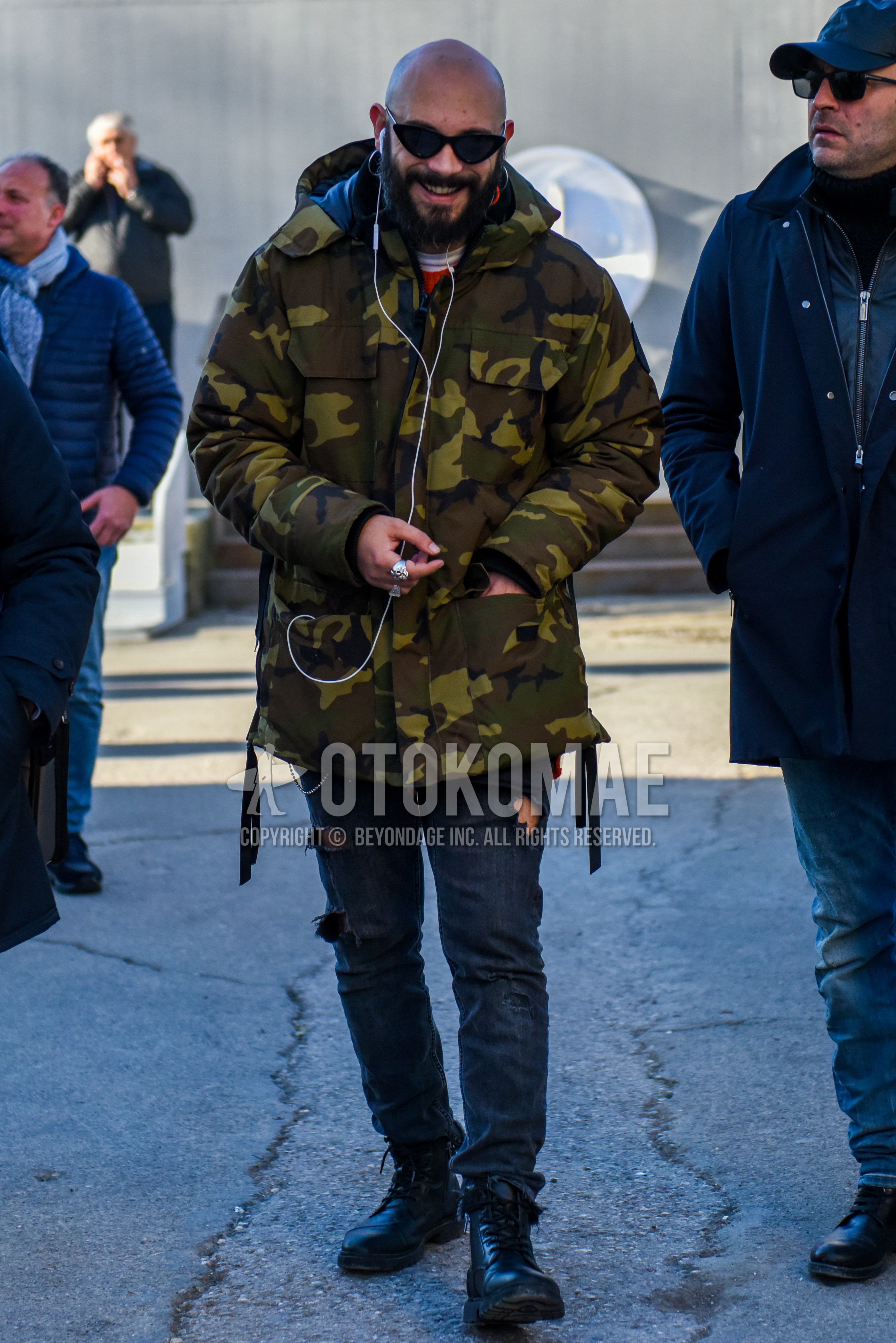 Men's winter outfit with plain sunglasses, olive green camouflage down jacket, dark gray plain damaged jeans, black  boots.