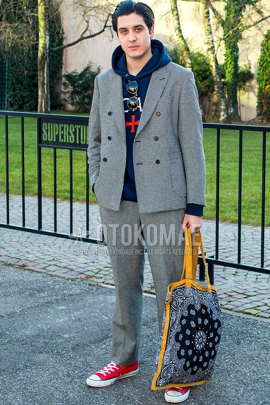 Men's autumn winter outfit with navy plain hoodie, red low-cut sneakers, paisley tote bag, gray plain suit.
