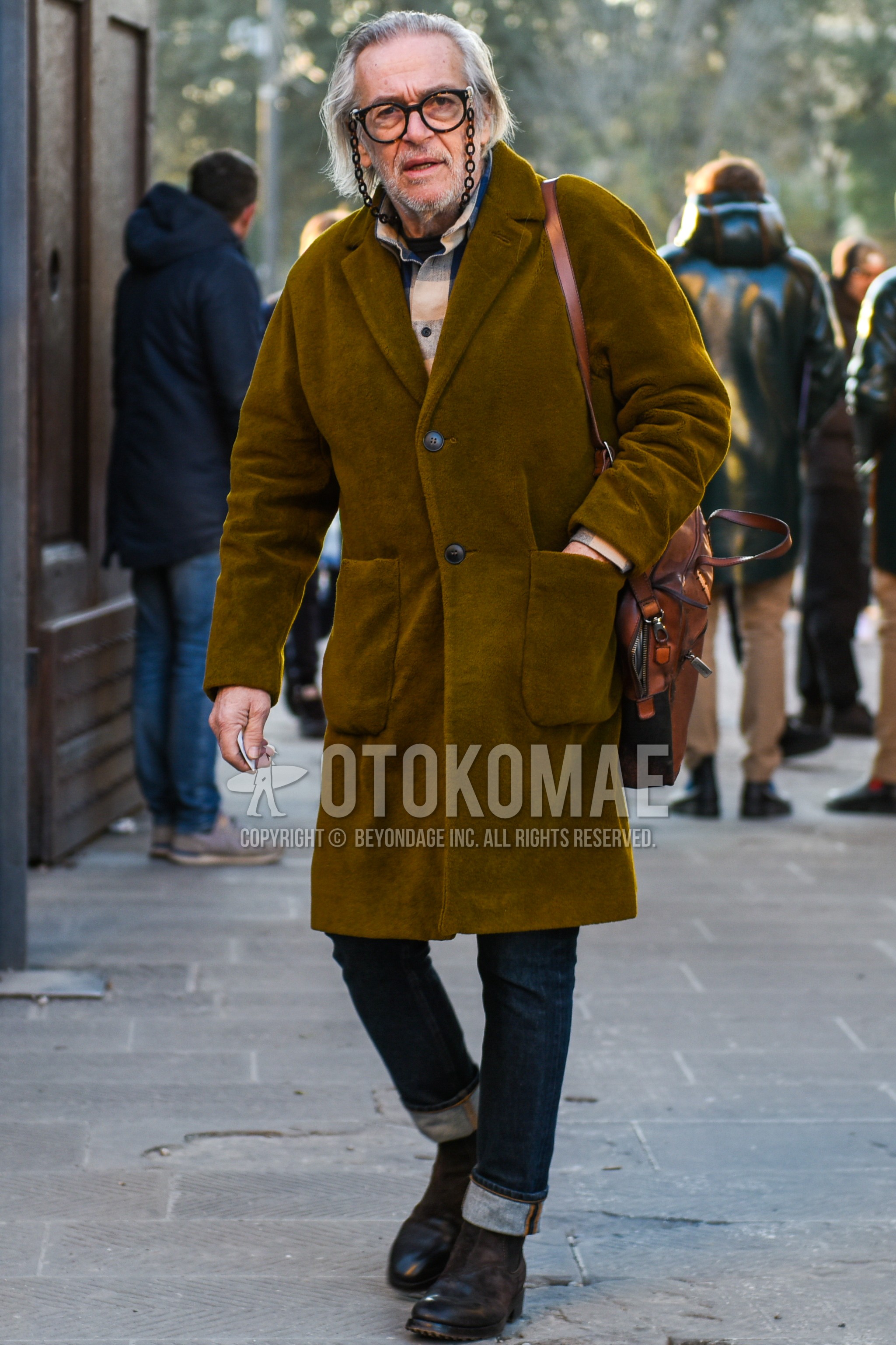 Men's autumn winter outfit with black plain glasses, beige plain chester coat, multi-color check shirt, blue plain denim/jeans, brown side-gore boots, brown plain shoulder bag.