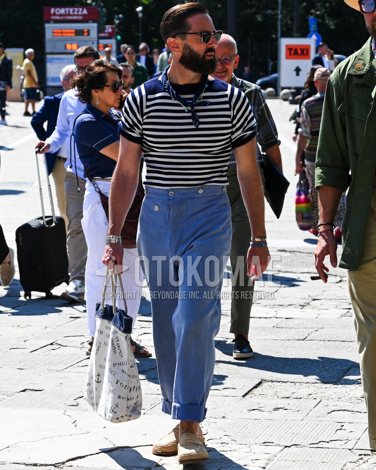 Men's spring summer outfit with black plain sunglasses, navy whole pattern bandana/neckerchief, navy horizontal stripes t-shirt, light blue plain slacks, beige coin loafers leather shoes, white whole pattern tote bag.