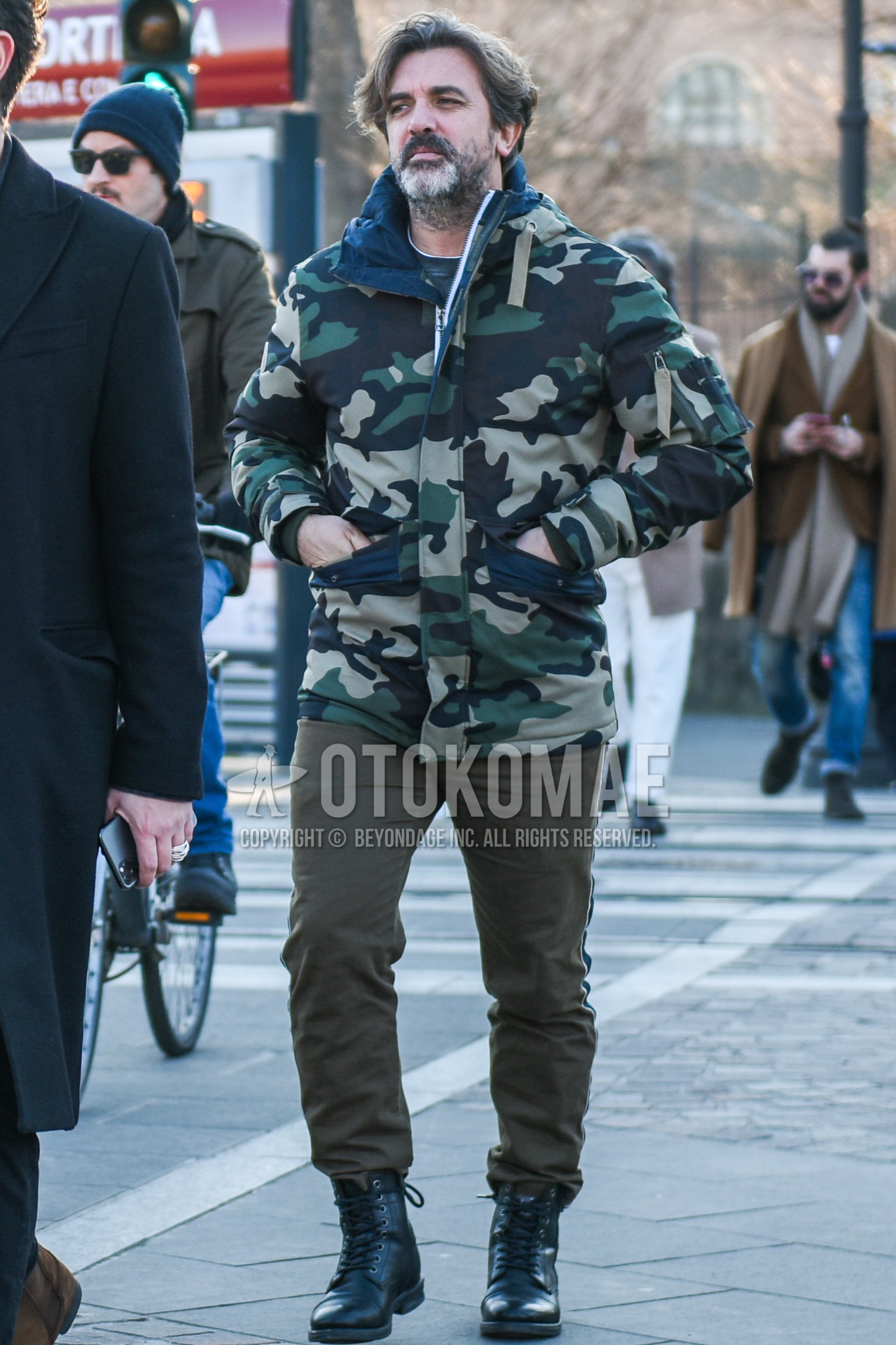 Men's autumn winter outfit with olive green camouflage windbreaker, beige plain chinos, black  boots.
