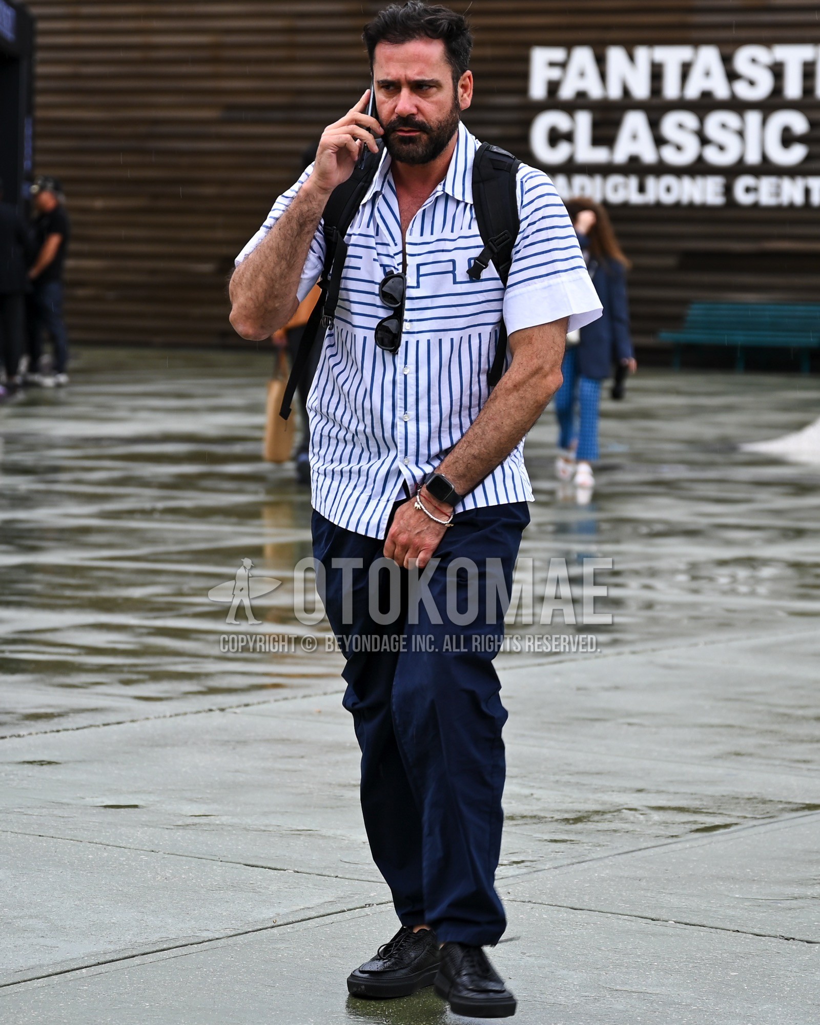 Men's spring summer outfit with white stripes shirt, navy plain chinos, black moccasins/deck shoes leather shoes, black plain backpack.