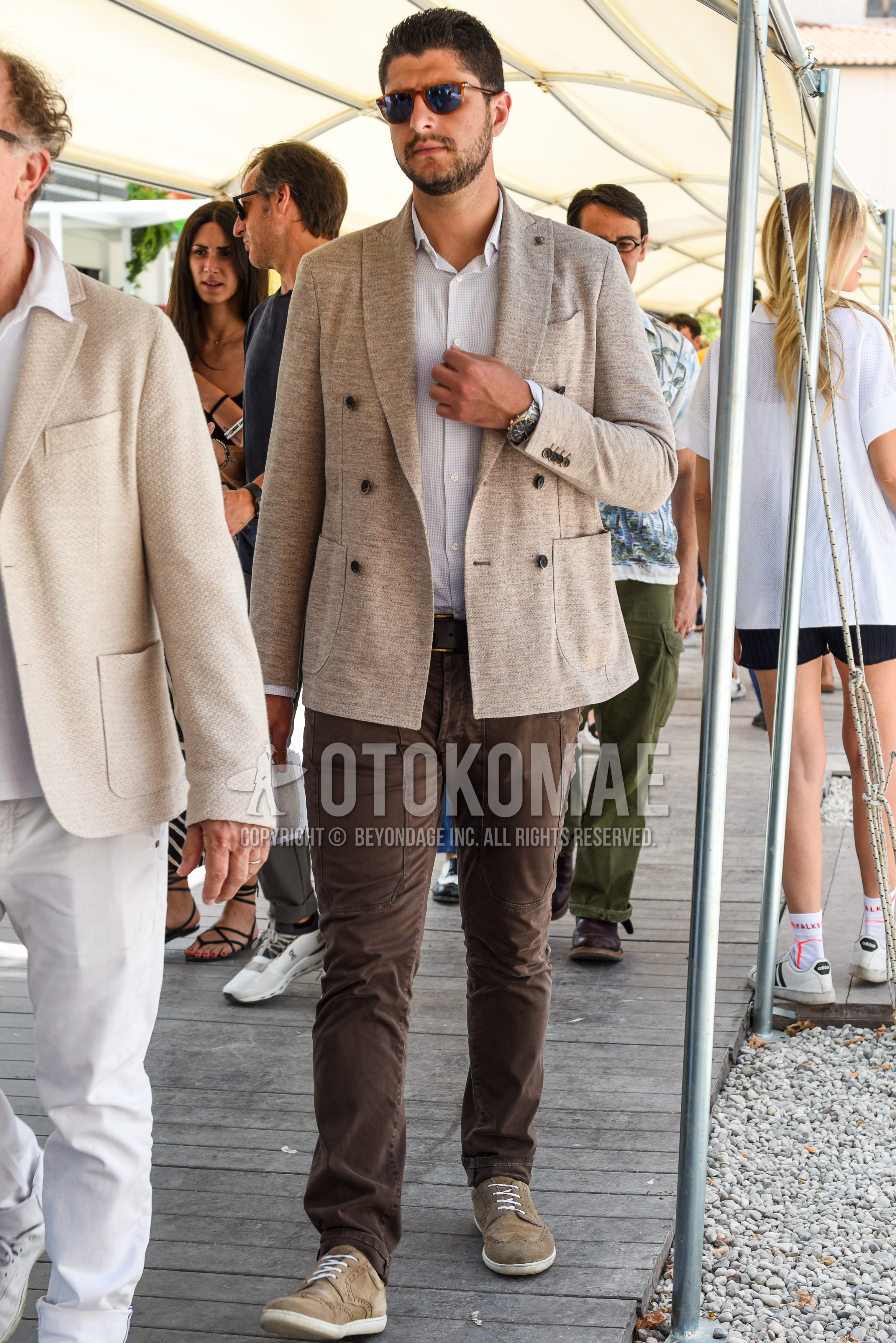 Men's spring summer outfit with brown tortoiseshell sunglasses, beige plain tailored jacket, white check shirt, brown plain leather belt, brown plain chinos, beige wing-tip shoes leather shoes.