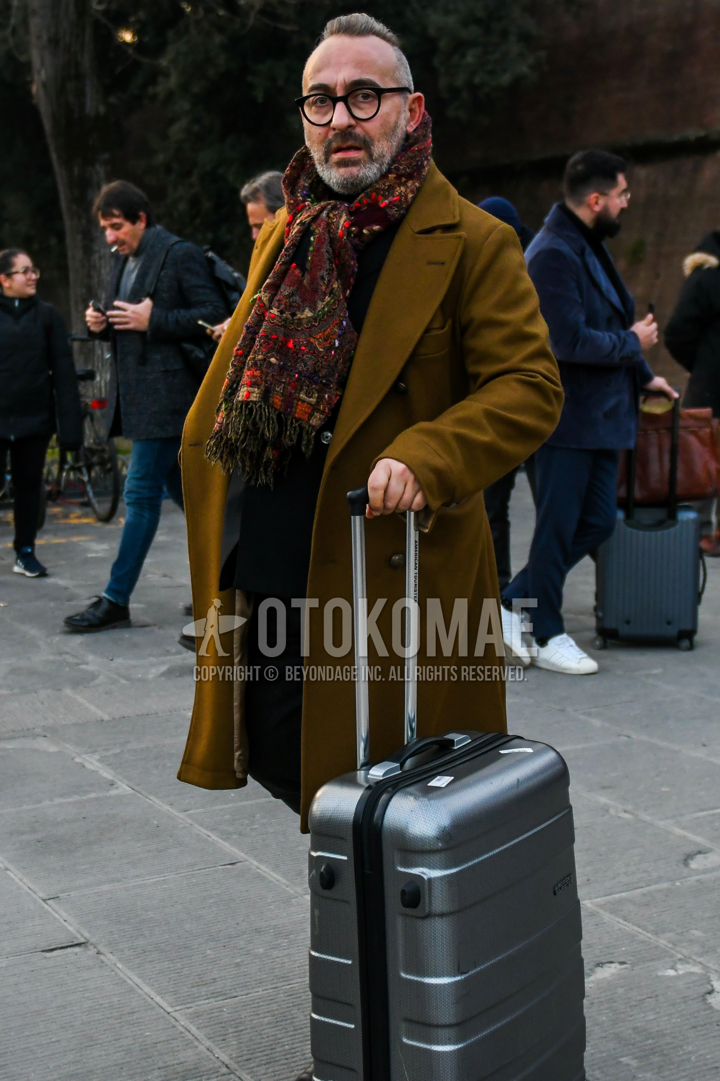 Men's winter outfit with beige plain glasses, brown scarf scarf, brown plain chester coat, gray plain suitcase.